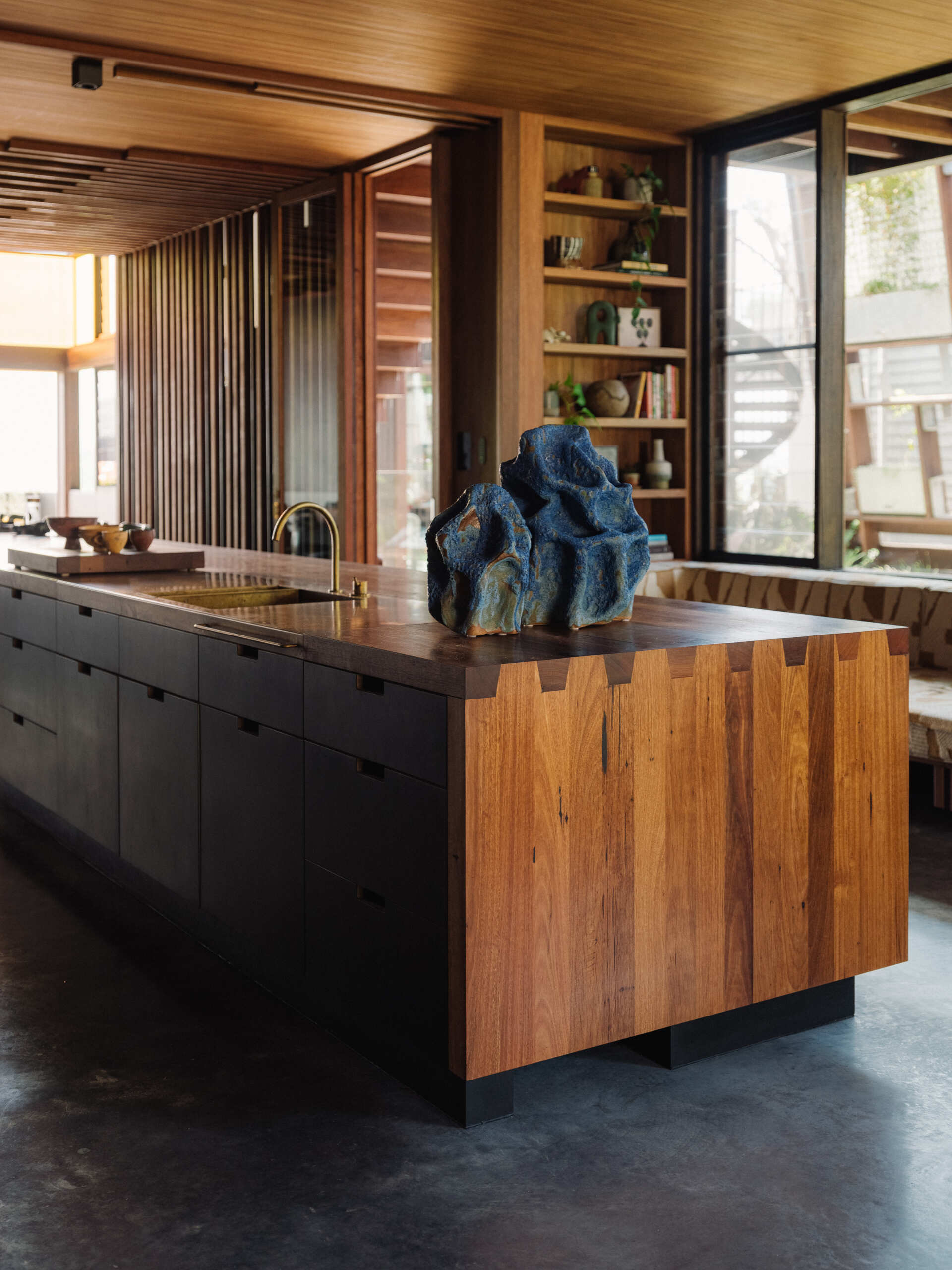 A 9.2 metre recycled hardwood island, which doubles as the dining table, stretches through to the kitchen. A full wall of cabinetry made from Paperock creates small niches that mimic dappled forest light, and offers generous storage without visual clutter. 