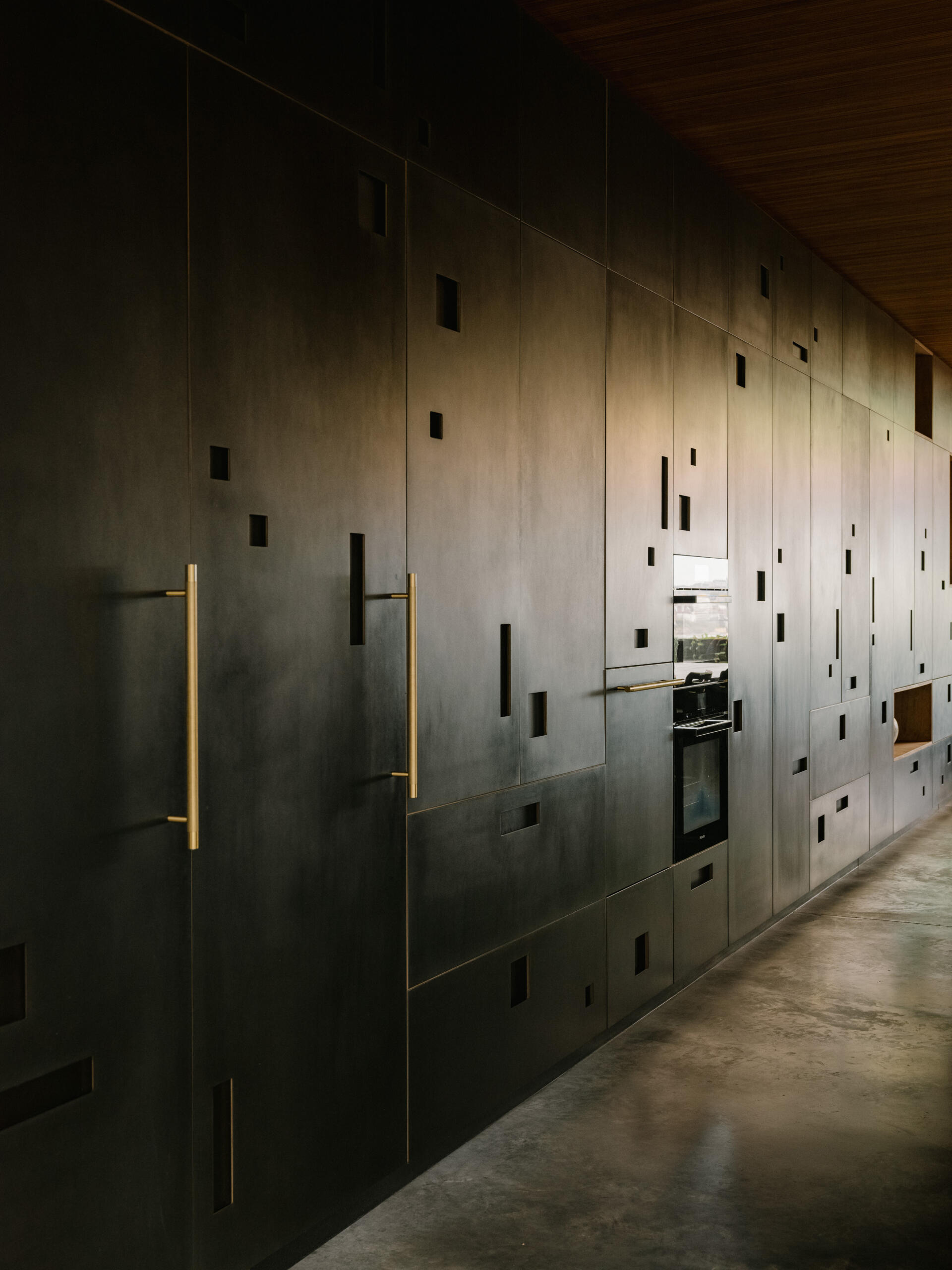 A 9.2 metre recycled hardwood island, which doubles as the dining table, stretches through to the kitchen. A full wall of cabinetry made from Paperock creates small niches that mimic dappled forest light, and offers generous storage without visual clutter. 