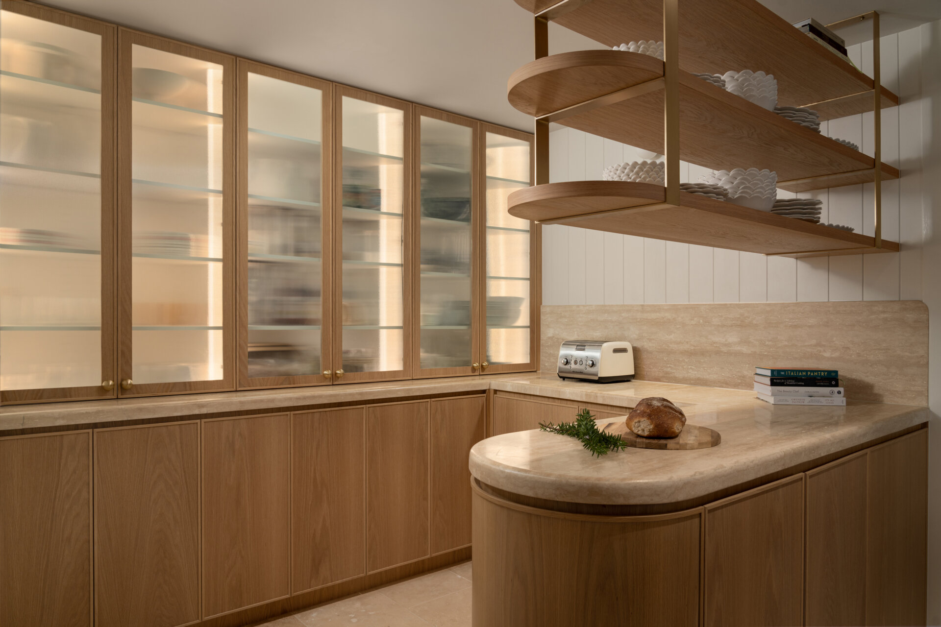 A travertine-rich kitchen with rounded, soft edges and a minimal Mediterranean palette. Nearby, a large walk-in pantry echoes the materials of the kitchen.