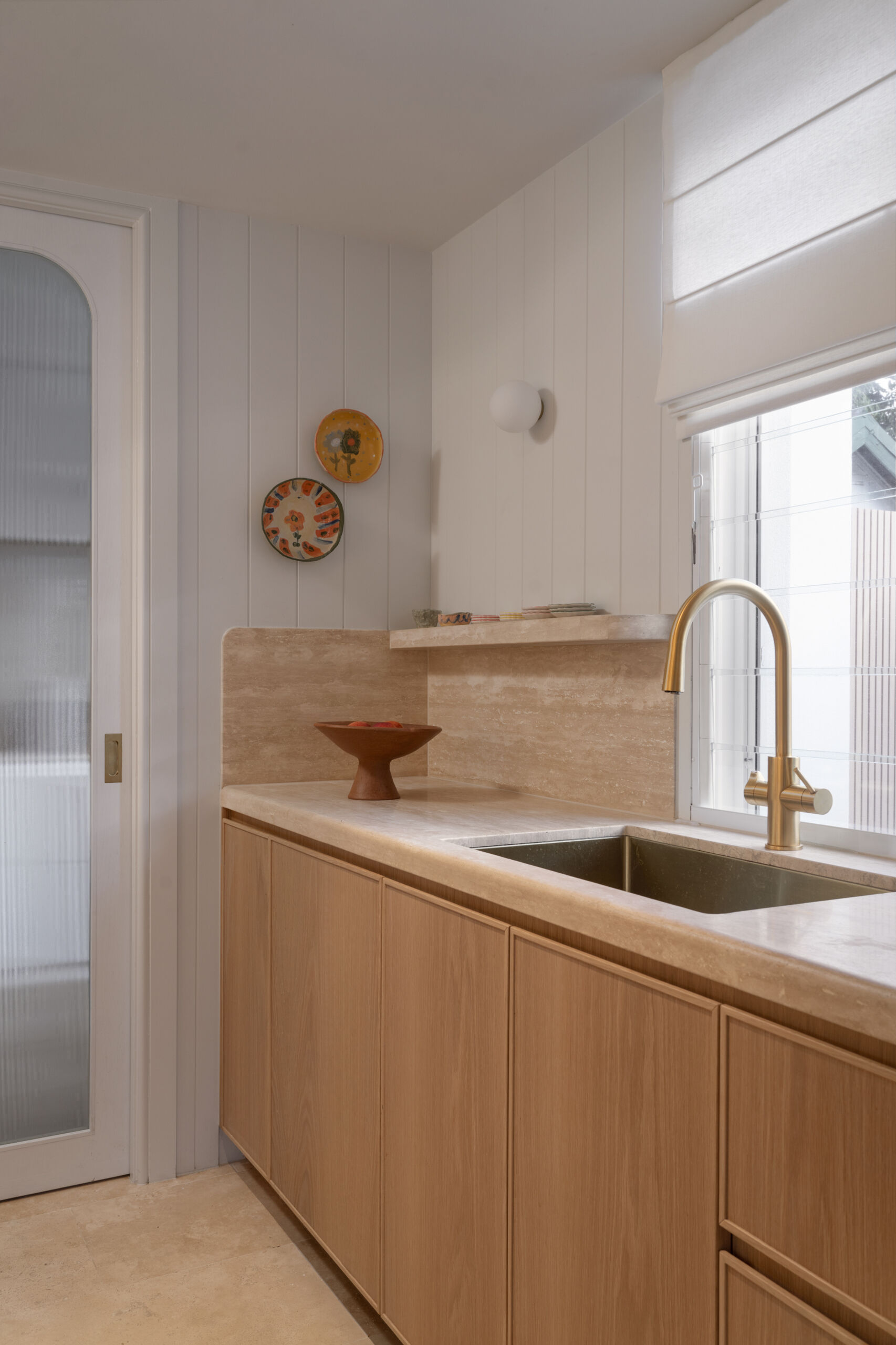 A travertine-rich kitchen with rounded, soft edges and a minimal Mediterranean palette. Nearby, a large walk-in pantry echoes the materials of the kitchen.