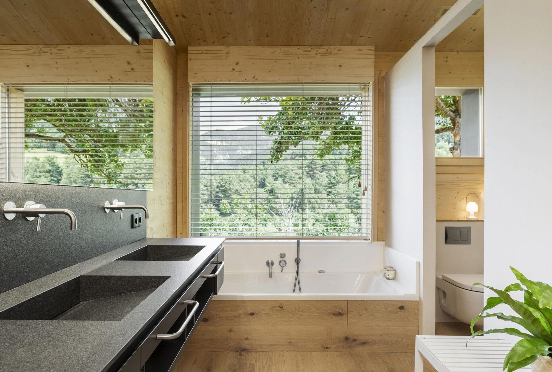 In the primary bathroom, a built-in bathtub sits beneath a window, inviting light and views into the room. Behind a partial wall, the toilet and shower are discreetly tucked away, preserving a clean and uncluttered layout.