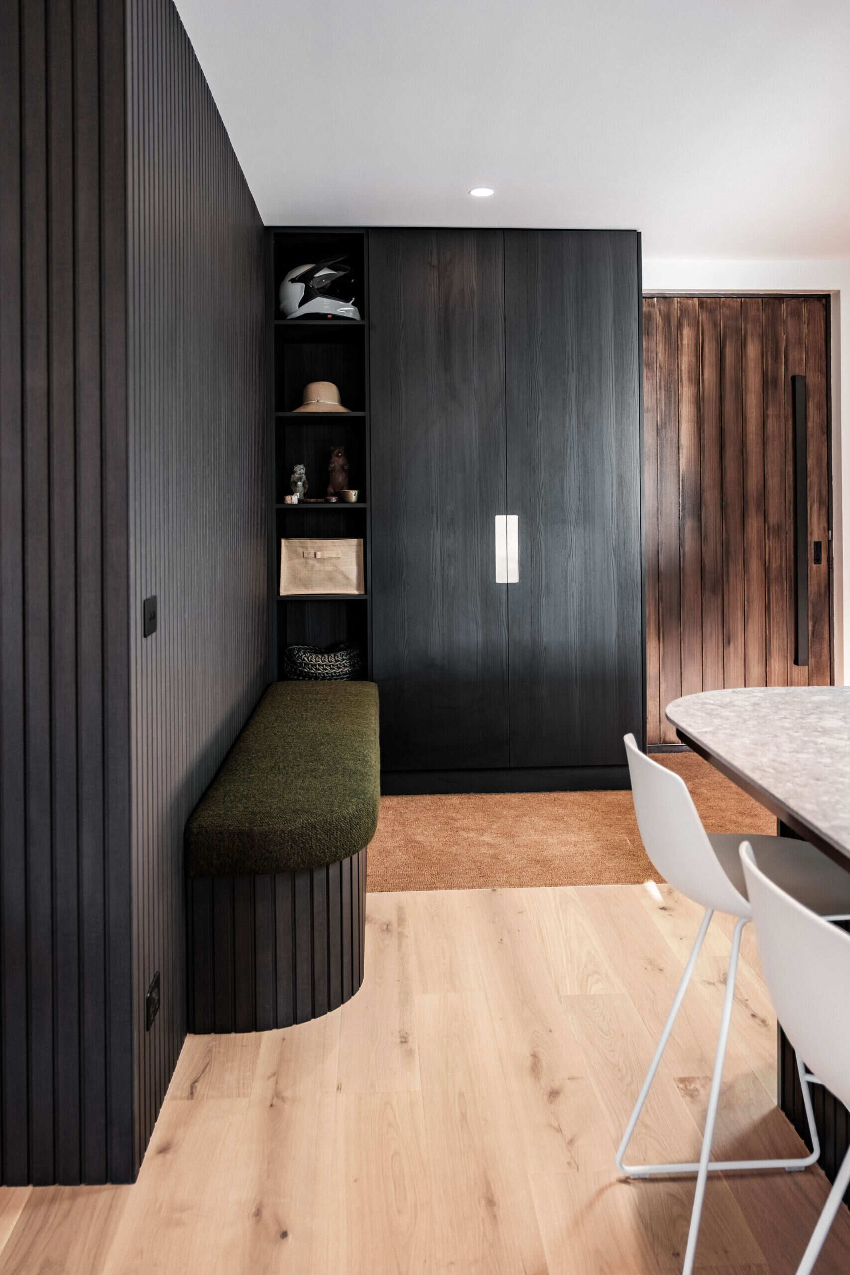 A welcoming entryway with custom joinery, a built in bench and textured black wall panelling that sets the tone for the home.