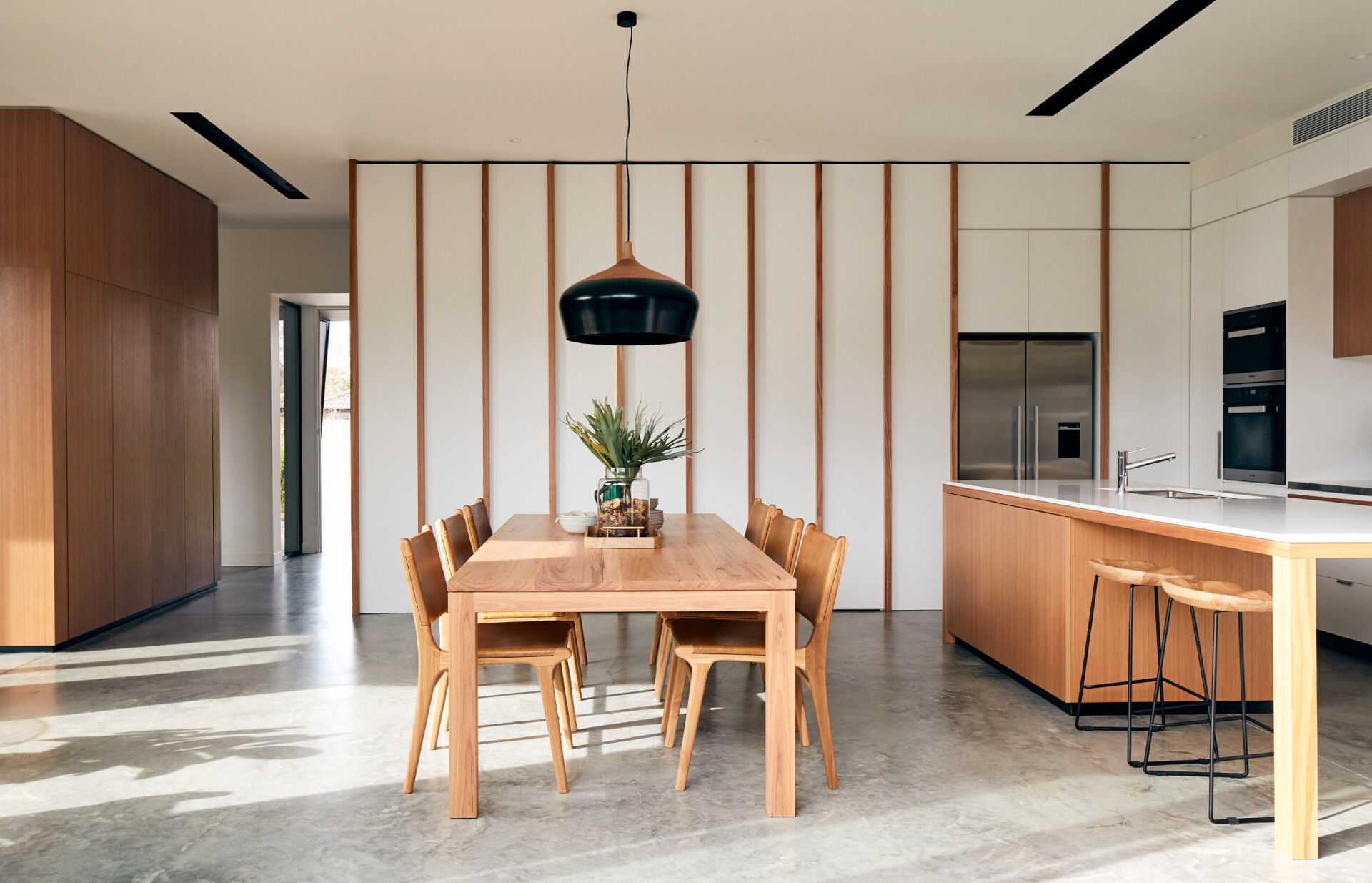 Light wood cabinetry and furniture soften the bright white kitchen and dining space.