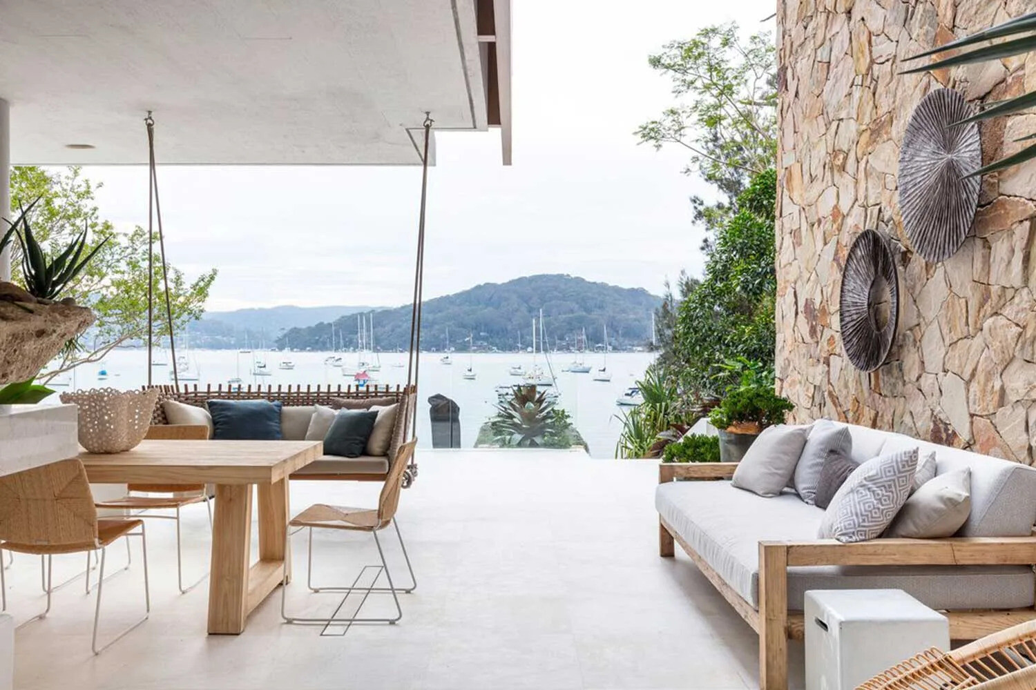 Covered outdoor lounge features a ceiling swing and sandstone accent wall, blending comfort, privacy and connection to nature.