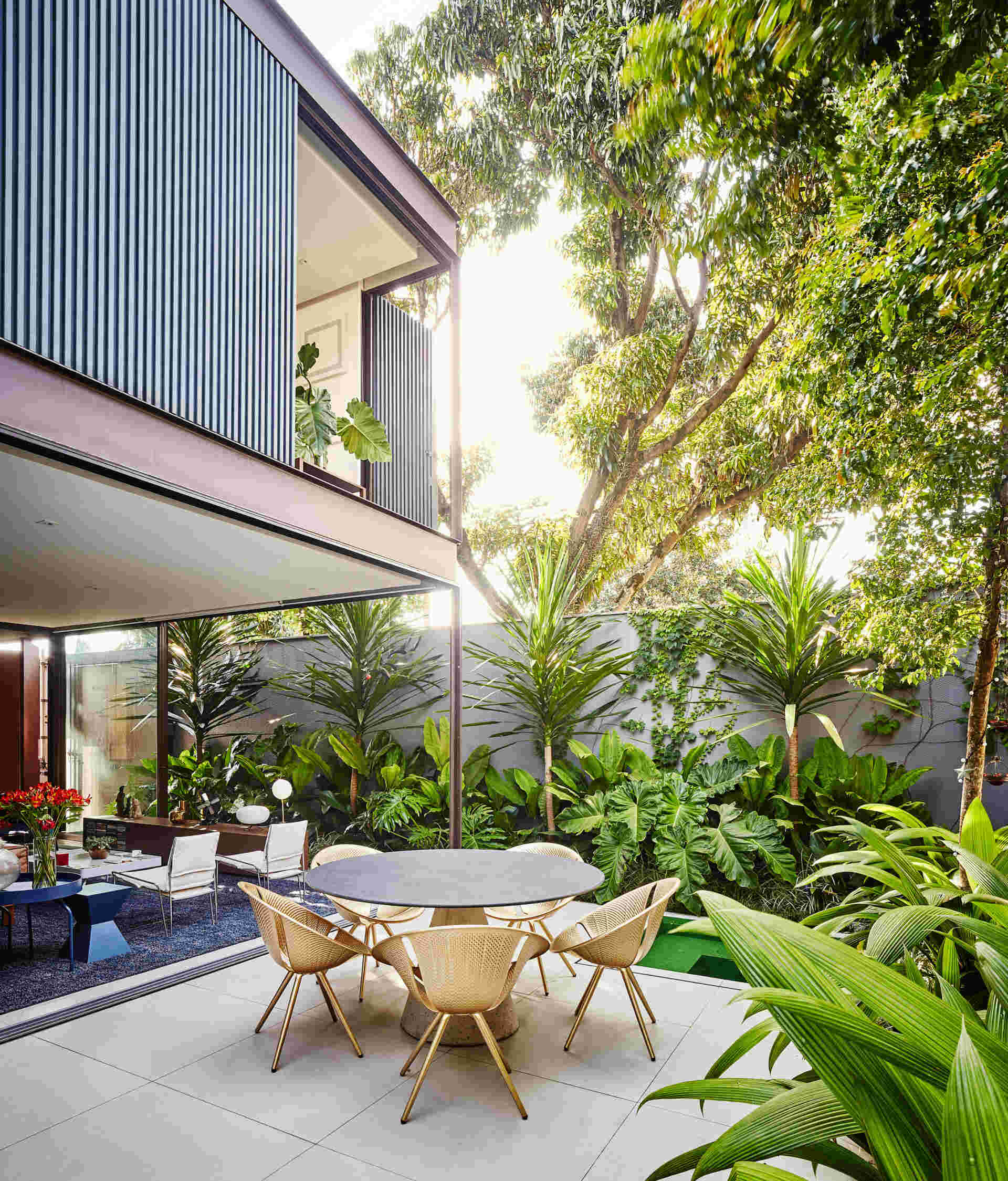 From the garden, the second floor becomes a defining feature. The upper level appears to hover above the ground floor, resting on a transparent base of glass. This contrast between the heavy opaque volume above and the lightness below gives the house its distinctive floating effect. Tropical landscaping surrounds the space, softening the concrete walls and bringing greenery deep into the home.