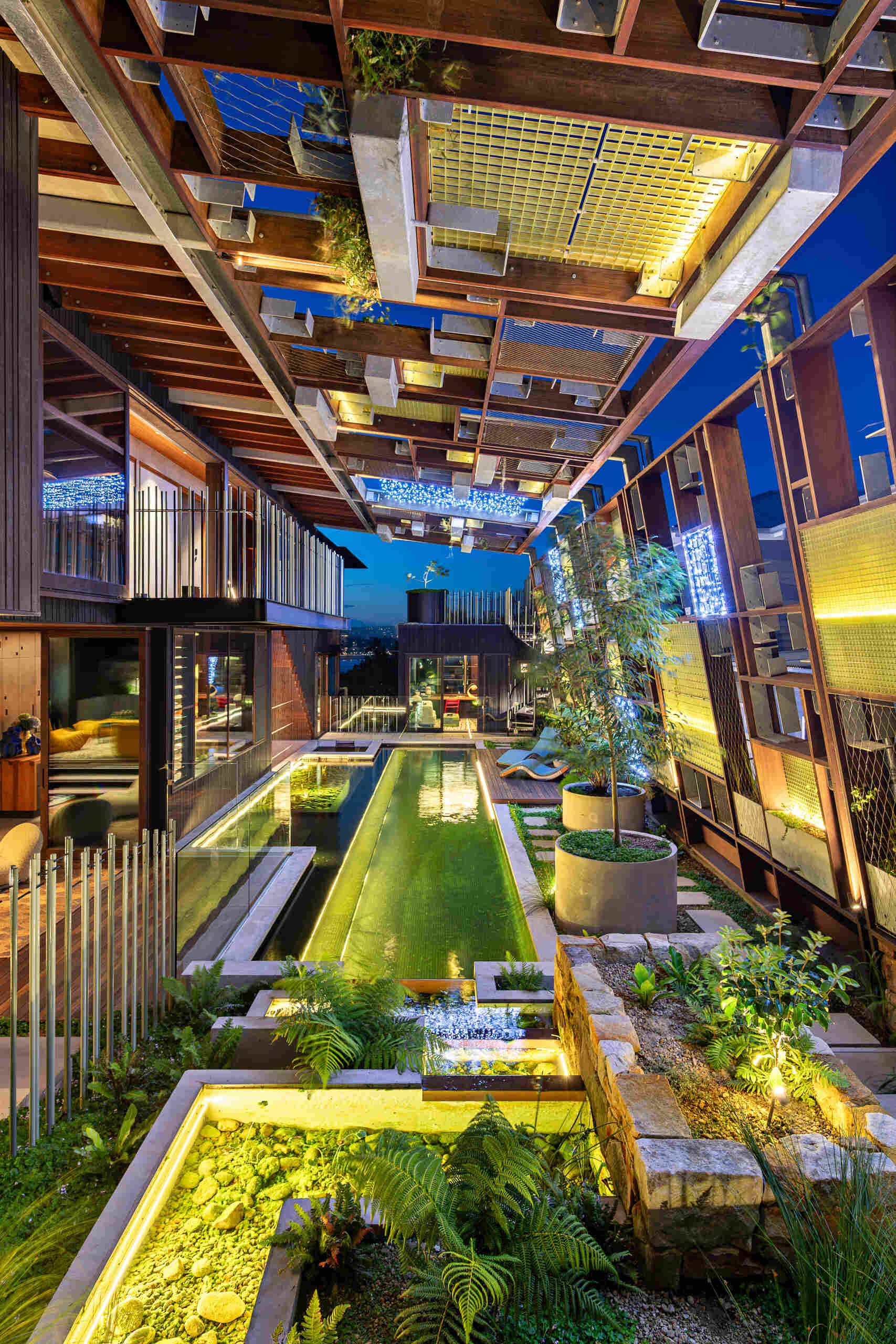 A natural swimming pool flows through the home beneath a canopy of plants and translucent FRP latticework.