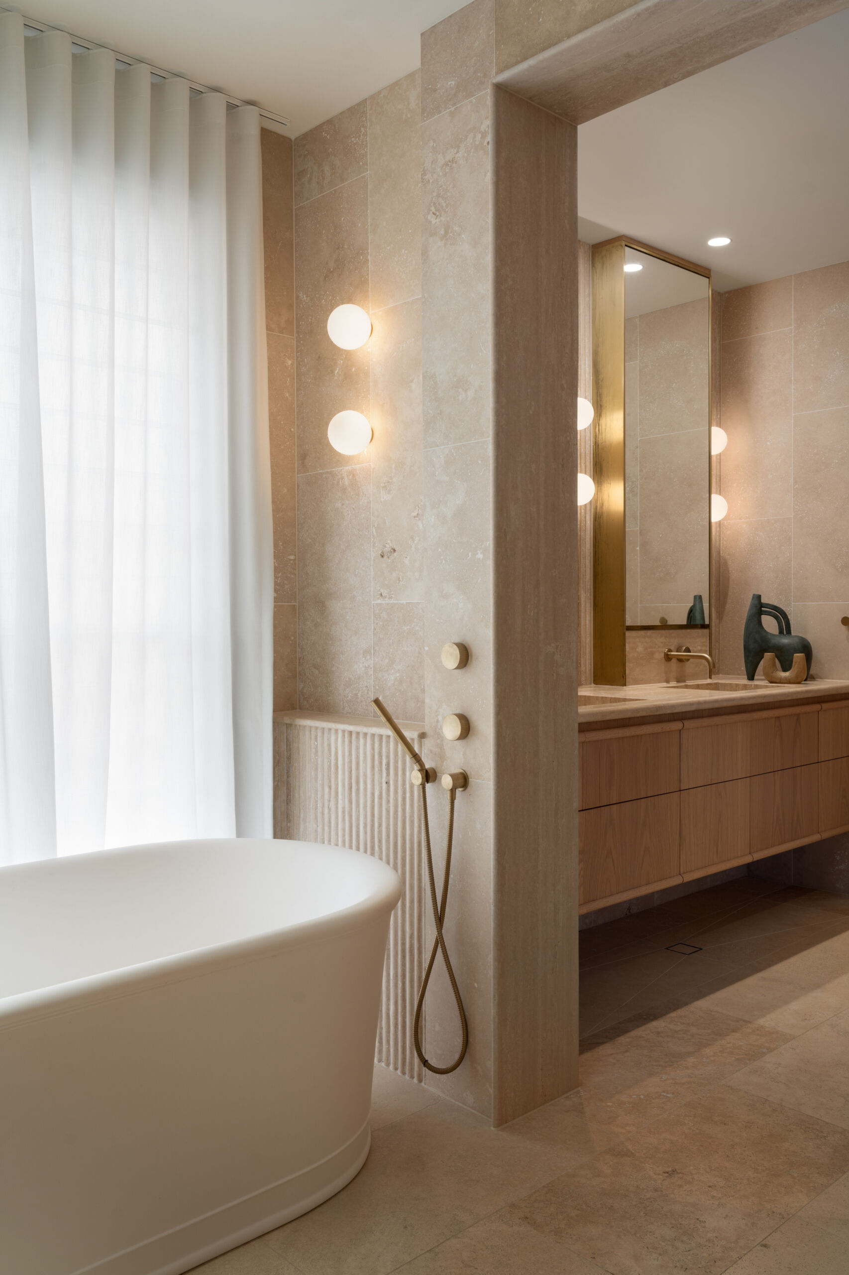 This en-suite bathroom turns the softer notes up a little further, using fluted stone with rounded edges to create visual interest while maintaining the spa-like serenity. Travertine remains the hero, divided into zones to give the space a sense of layered grandeur.