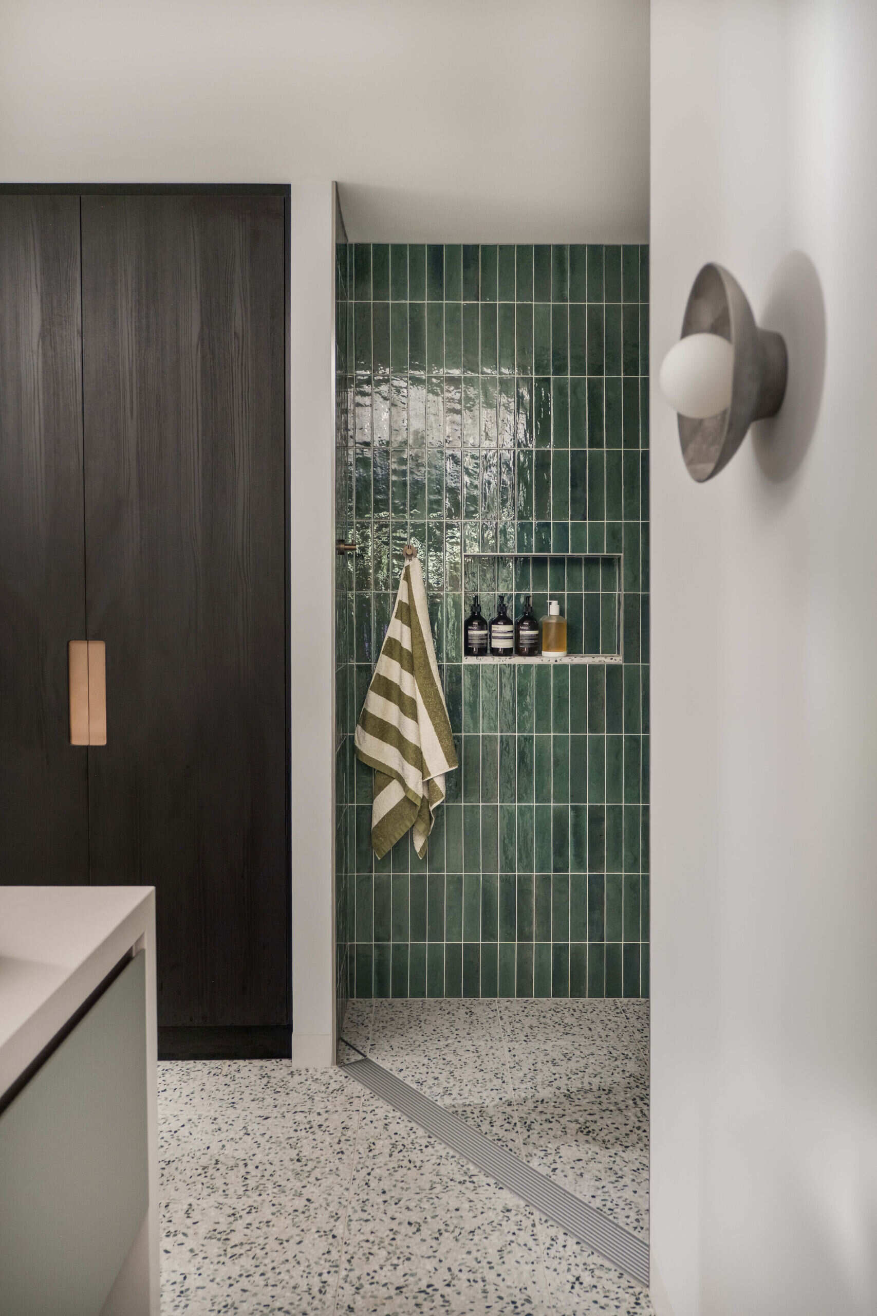A sculptural bathroom with a curved shower featuring emerald tiles, terrazzo floors and floating mirrors designed for an elevated daily experience.