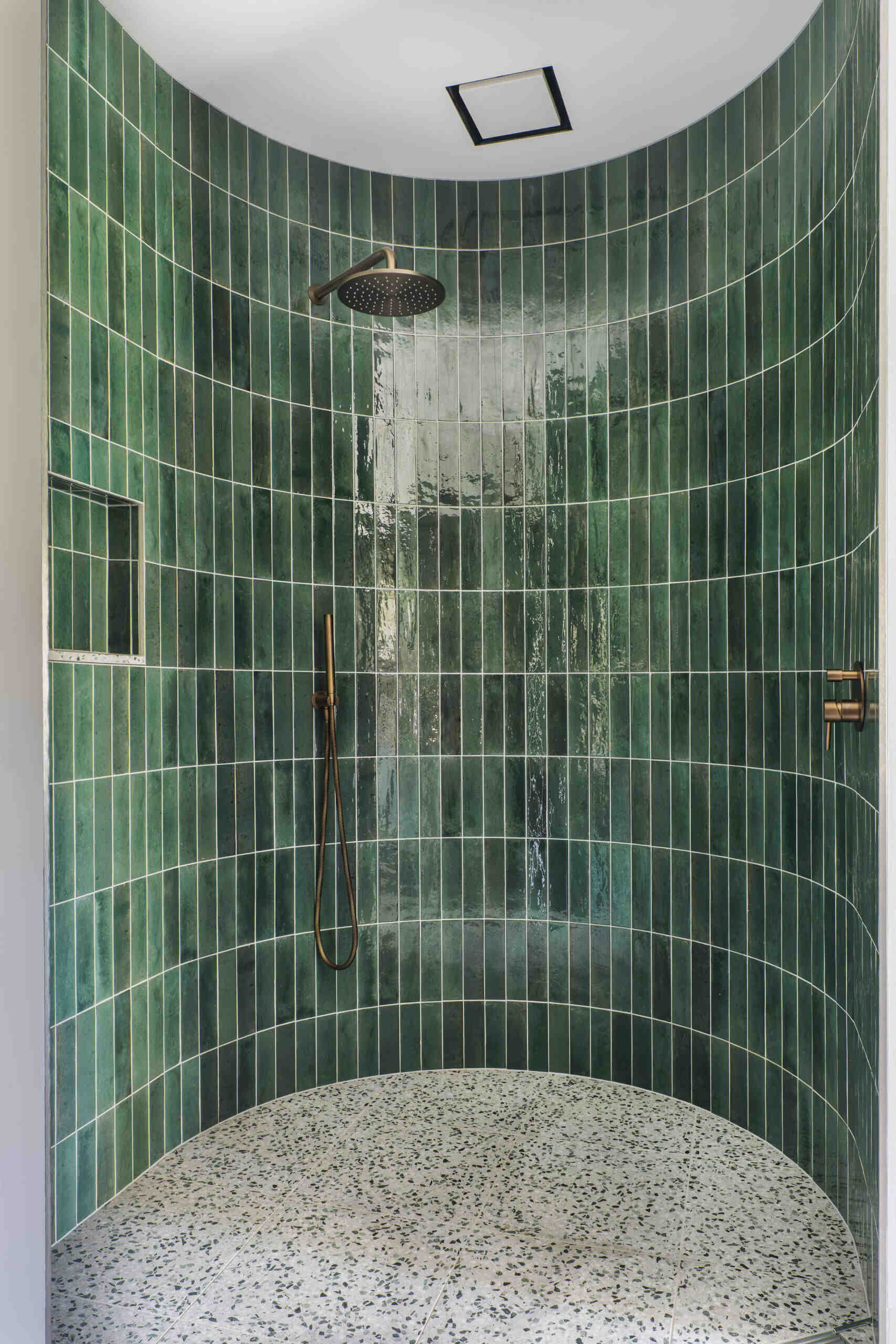 A sculptural bathroom with a curved shower featuring emerald tiles, terrazzo floors and floating mirrors designed for an elevated daily experience.