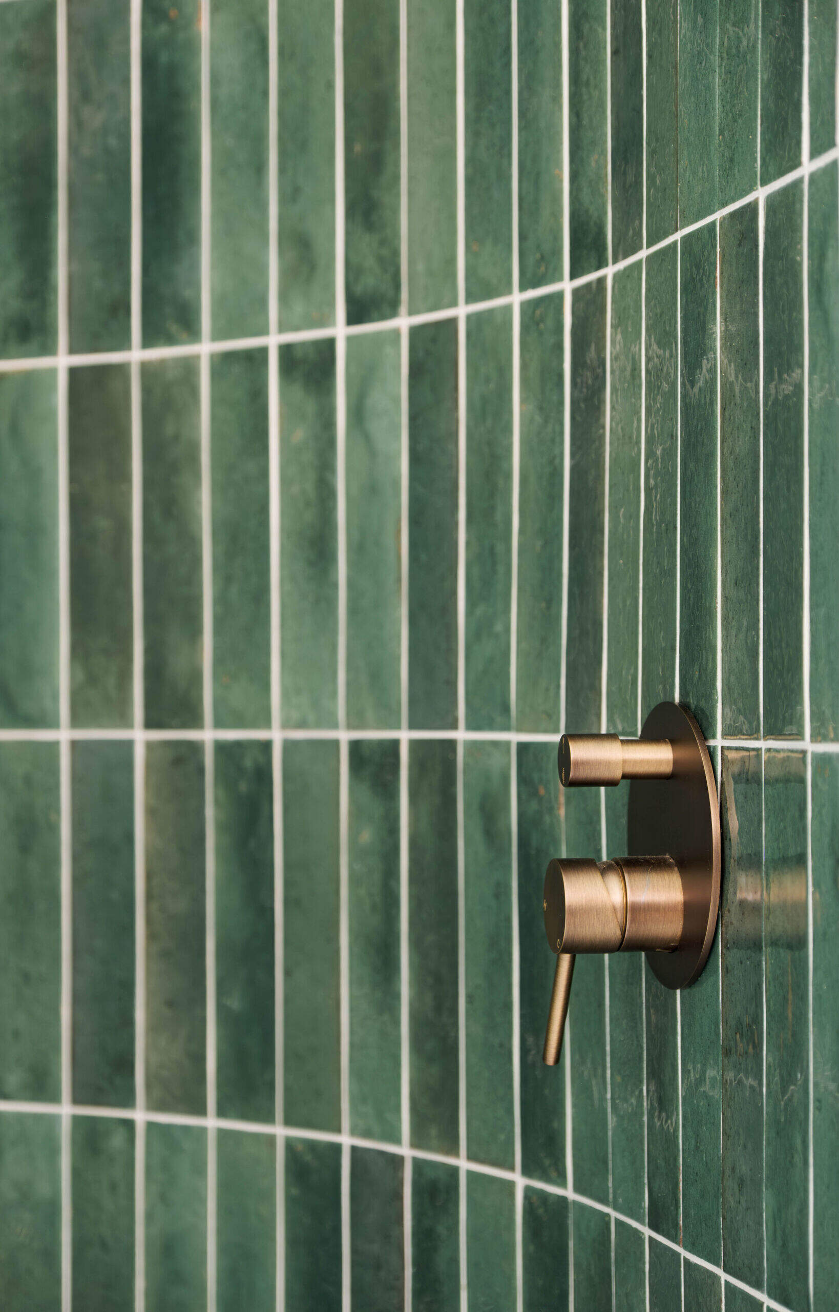 A sculptural bathroom with a curved shower featuring emerald tiles, terrazzo floors and floating mirrors designed for an elevated daily experience.