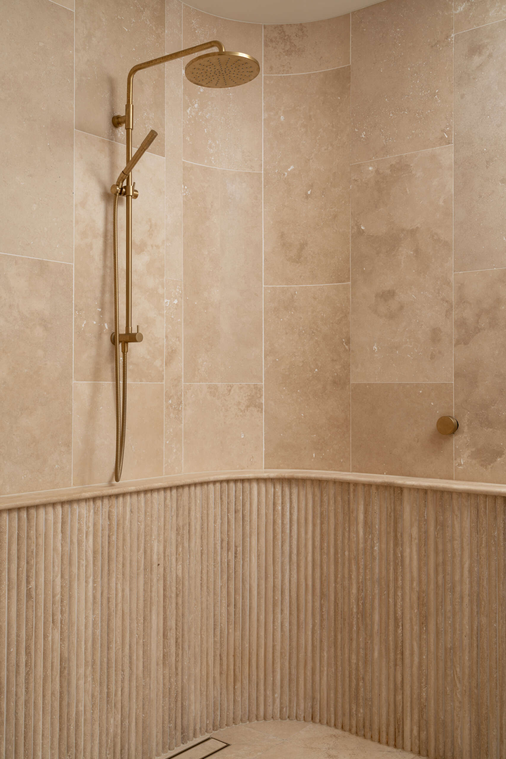 This en-suite bathroom turns the softer notes up a little further, using fluted stone with rounded edges to create visual interest while maintaining the spa-like serenity. Travertine remains the hero, divided into zones to give the space a sense of layered grandeur.