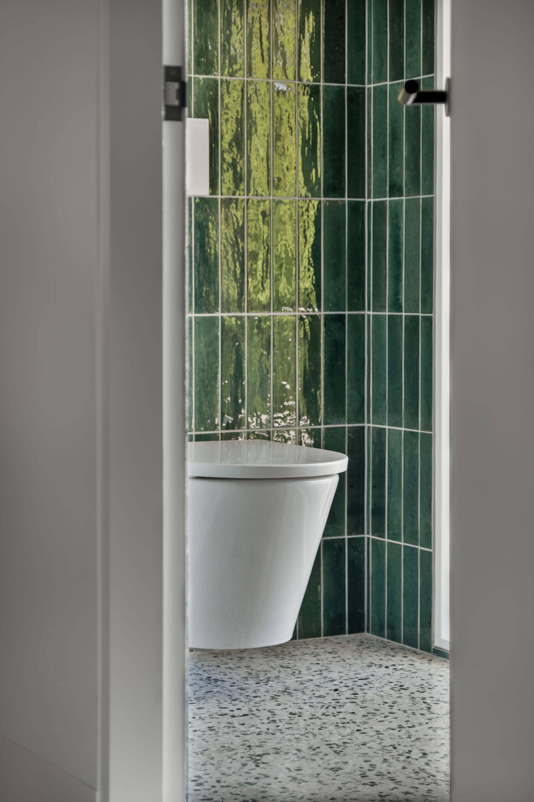 A sculptural bathroom with a curved shower featuring emerald tiles, terrazzo floors and floating mirrors designed for an elevated daily experience.
