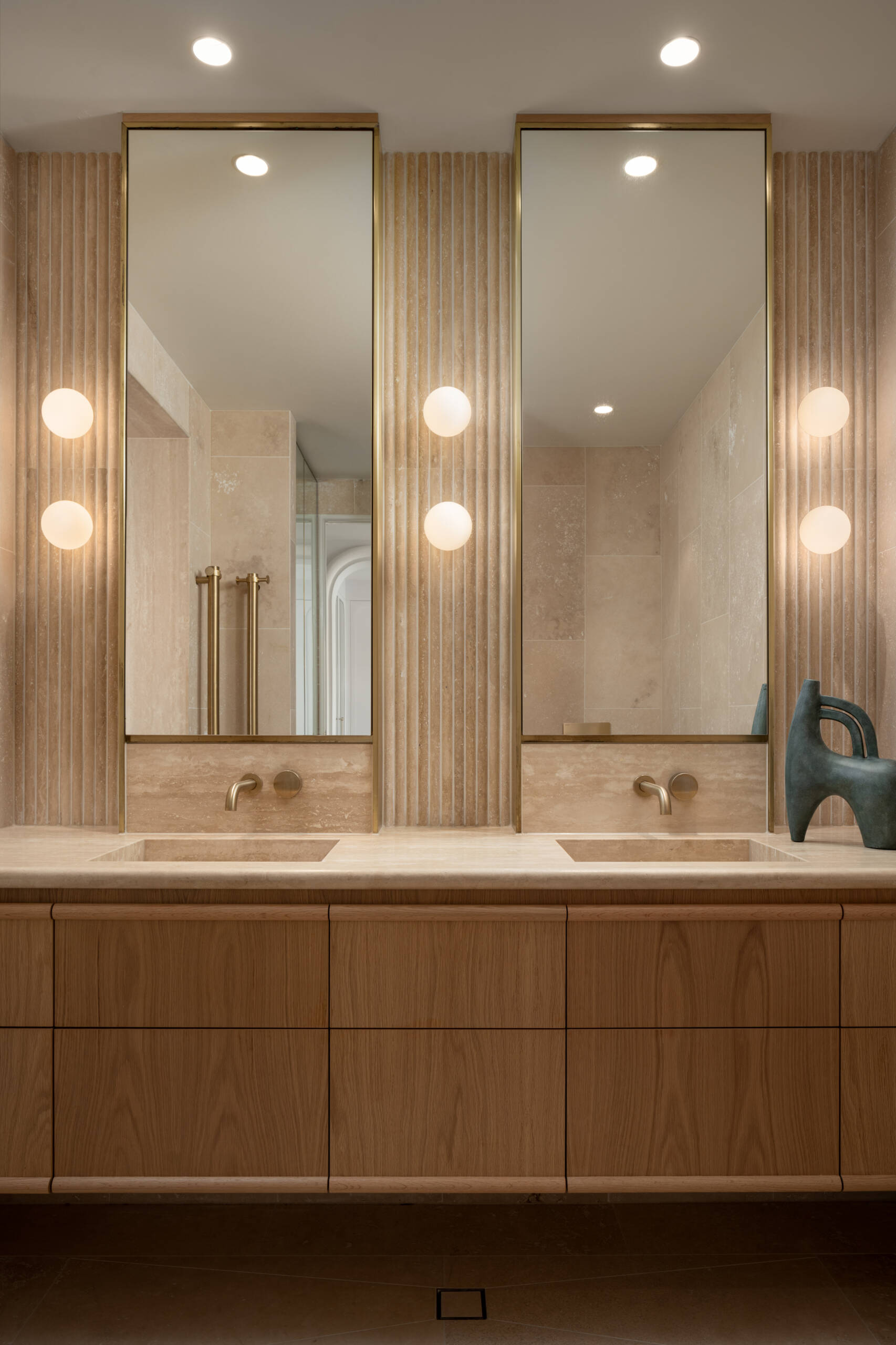 This en-suite bathroom turns the softer notes up a little further, using fluted stone with rounded edges to create visual interest while maintaining the spa-like serenity. Travertine remains the hero, divided into zones to give the space a sense of layered grandeur.