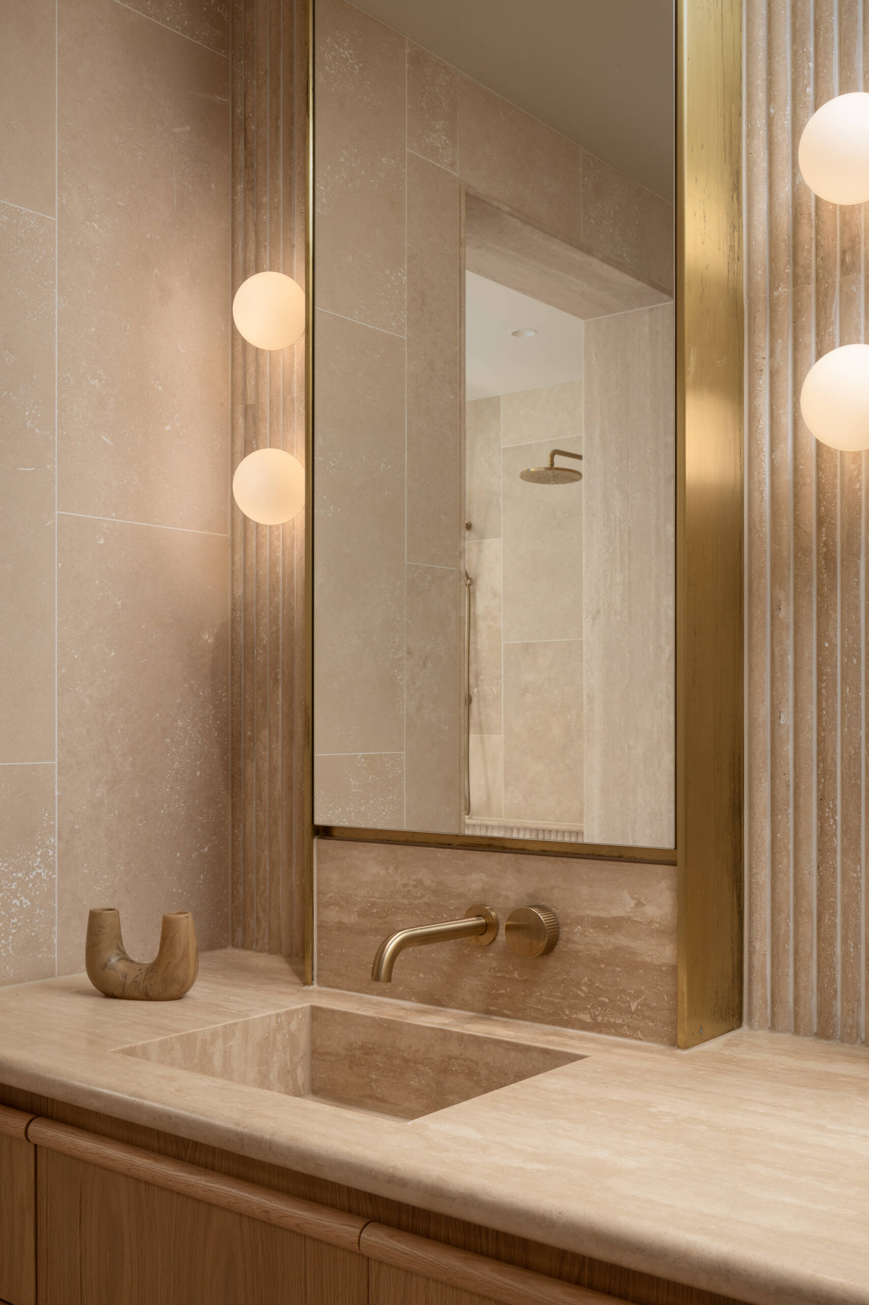 This en-suite bathroom turns the softer notes up a little further, using fluted stone with rounded edges to create visual interest while maintaining the spa-like serenity. Travertine remains the hero, divided into zones to give the space a sense of layered grandeur.