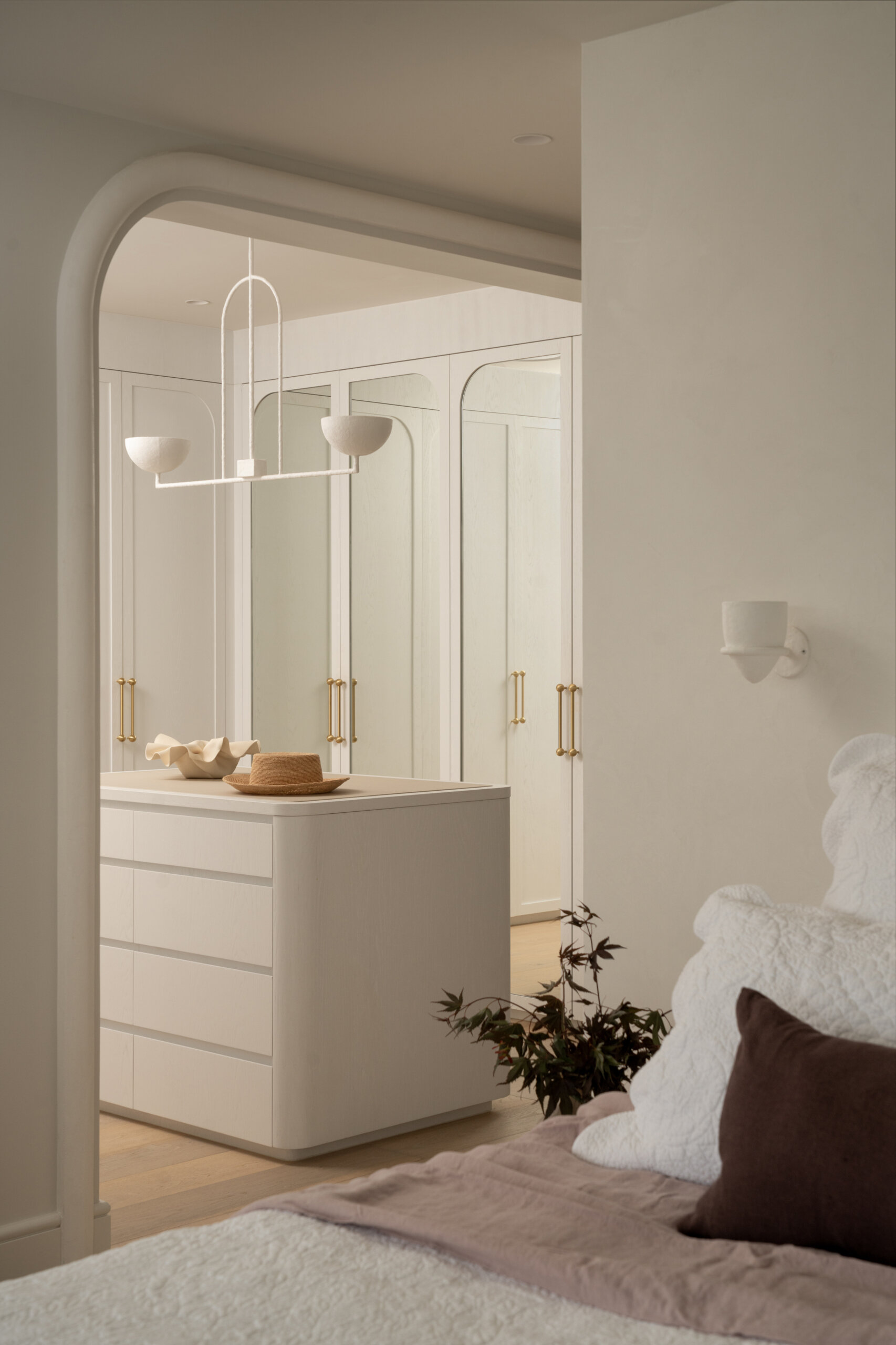 The primary suite is designed for unwinding. The bedroom stays understated and layered, with a calm presence that settles instantly. In the walk-in robe, a clean white scheme comes to life with warm lighting bouncing off subtle timber grain.