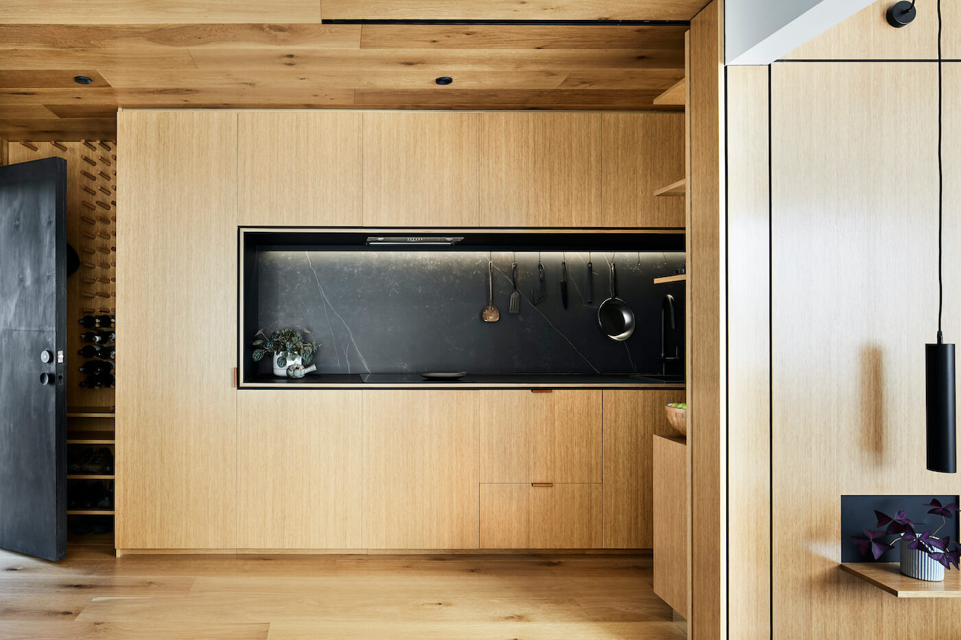 A long timber kitchen with black accents hides appliances and maximises bench space inside this compact Melbourne apartment.