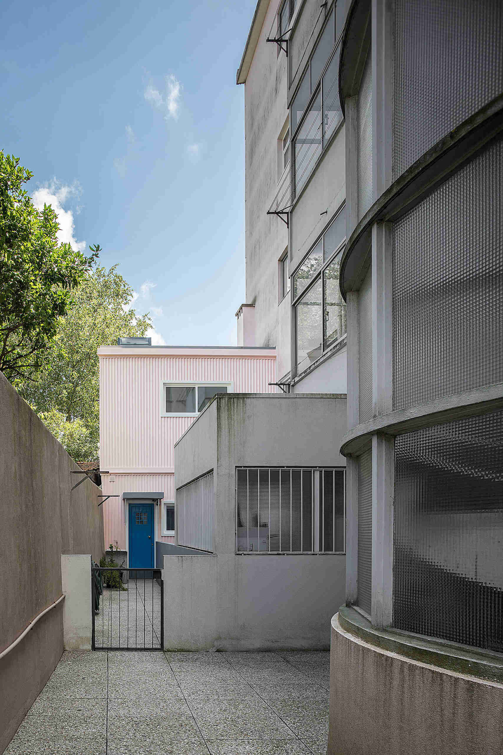 A thoughtfully renovated tiny house hidden behind a modernist building, has a pink exterior and soft blue interior.