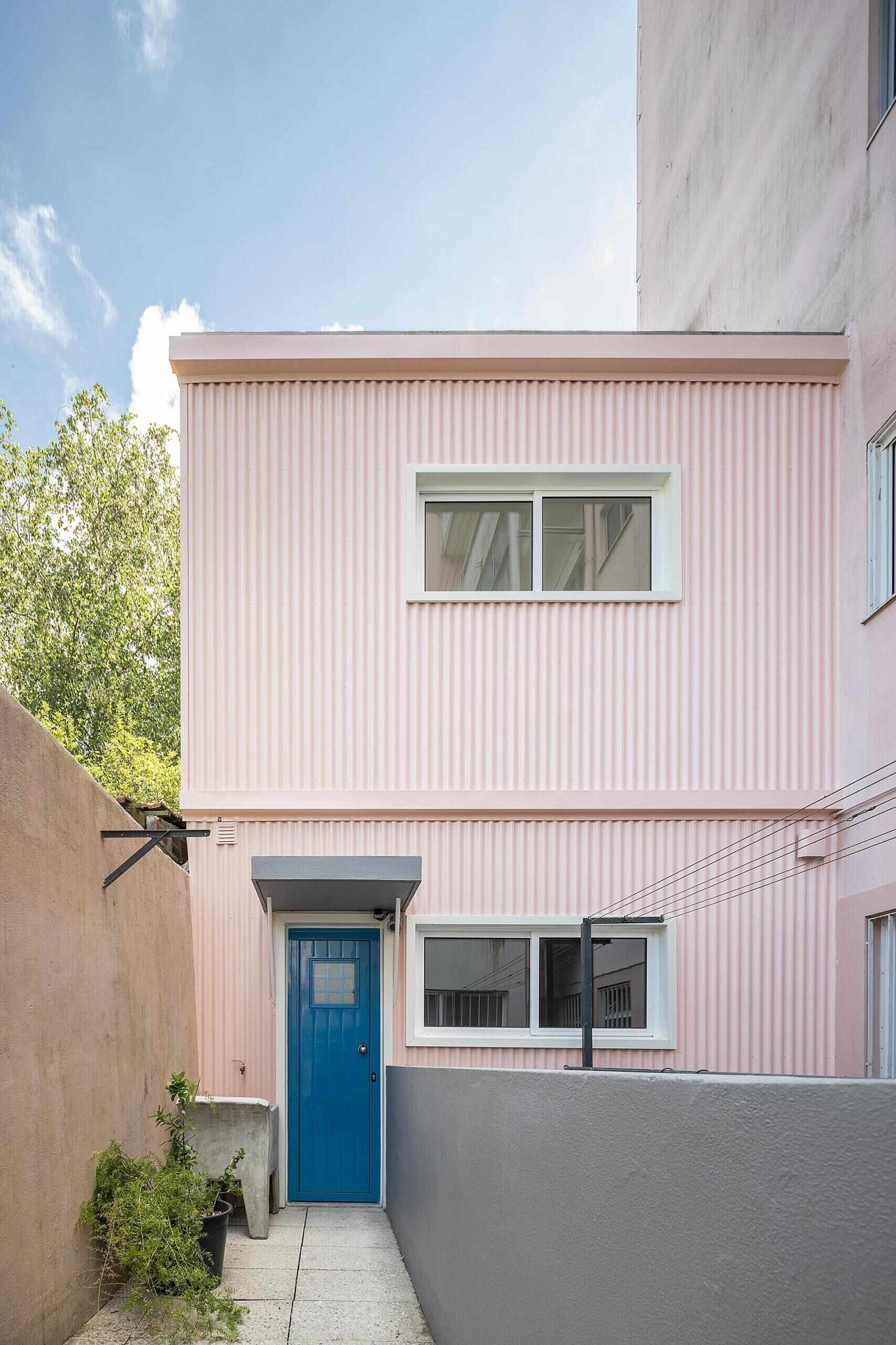 A thoughtfully renovated tiny house hidden behind a modernist building, has a pink exterior and soft blue interior.