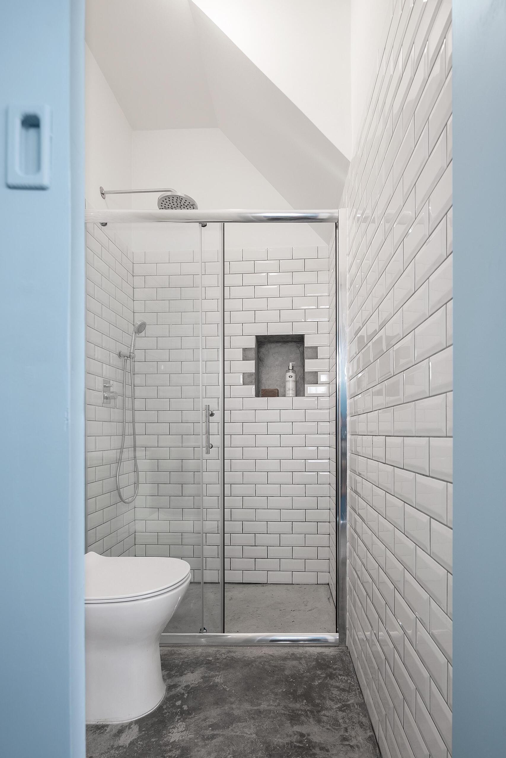 A tiny house bathroom in Porto featuring white subway tiles, a built-in shower shelf, and a corner basin that maximizes space without sacrificing style.