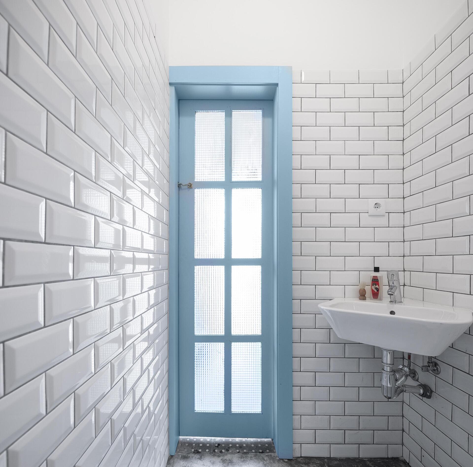 A tiny house bathroom in Porto featuring white subway tiles, a built-in shower shelf, and a corner basin that maximizes space without sacrificing style.