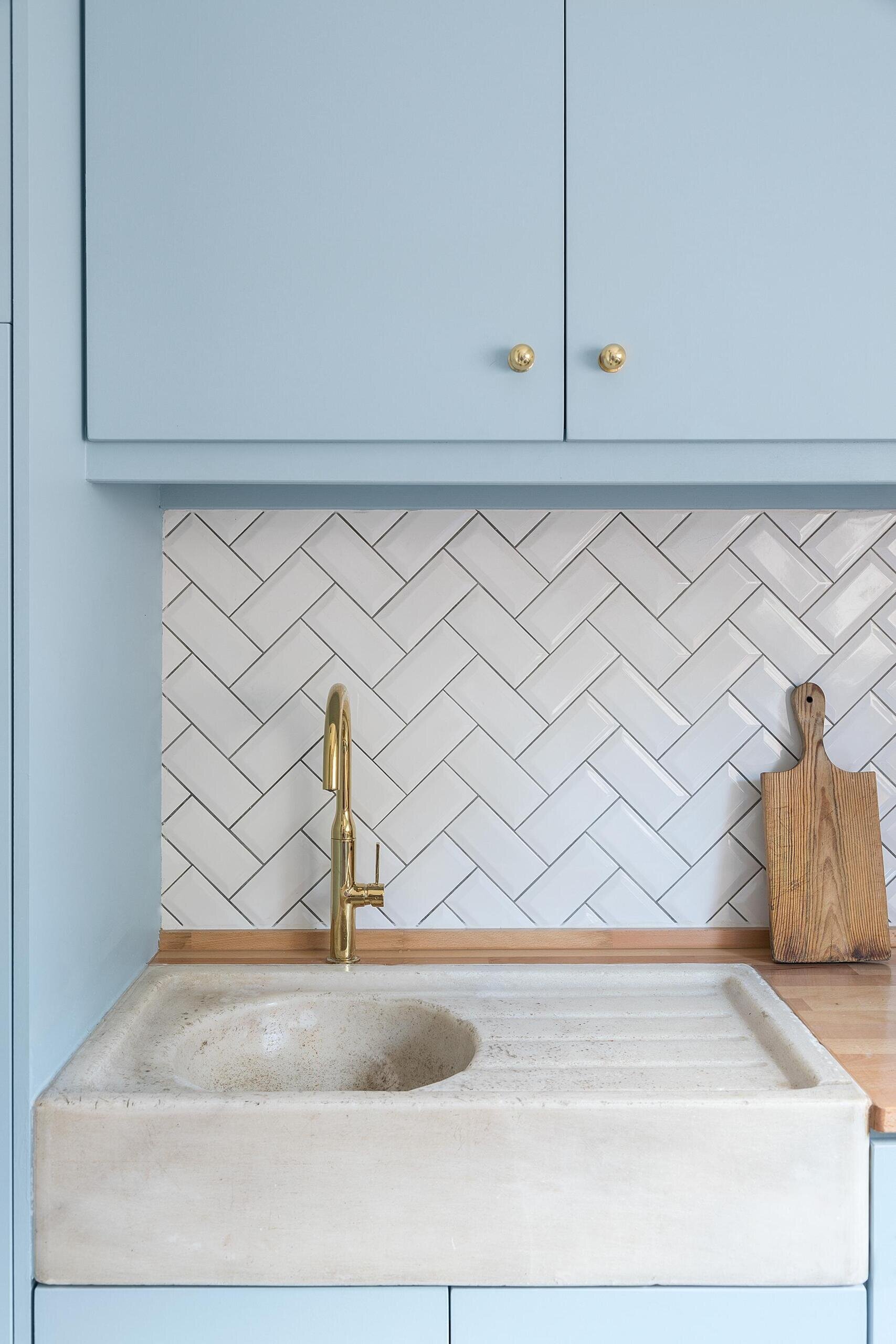 A compact kitchen with powder blue cabinets, wood countertops, and white herringbone subway tiles in a thoughtfully renovated tiny house.