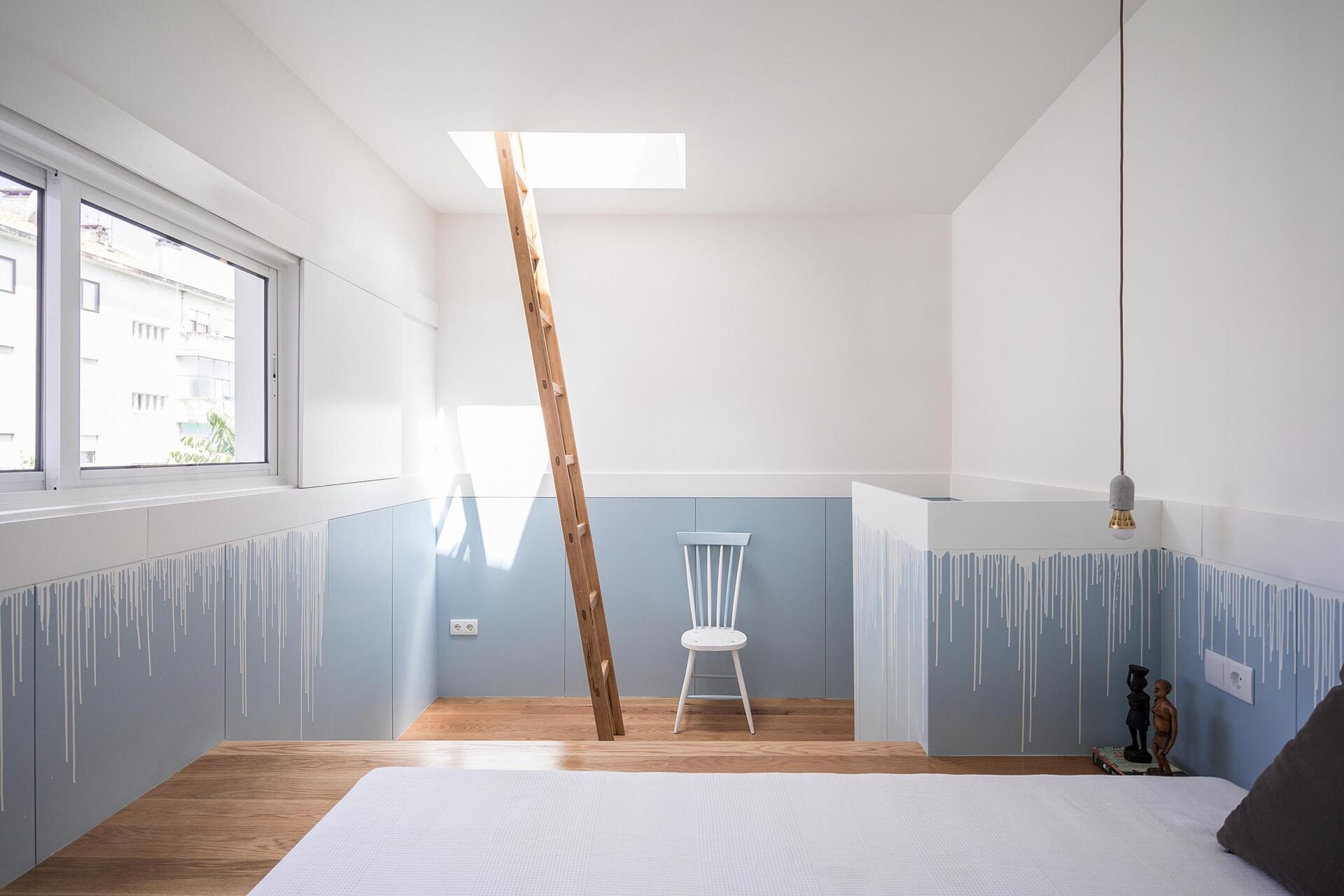 A tiny house bedroom with a raised wooden bed platform, built-in storage, and a soft blue and white drip-effect wall finish.