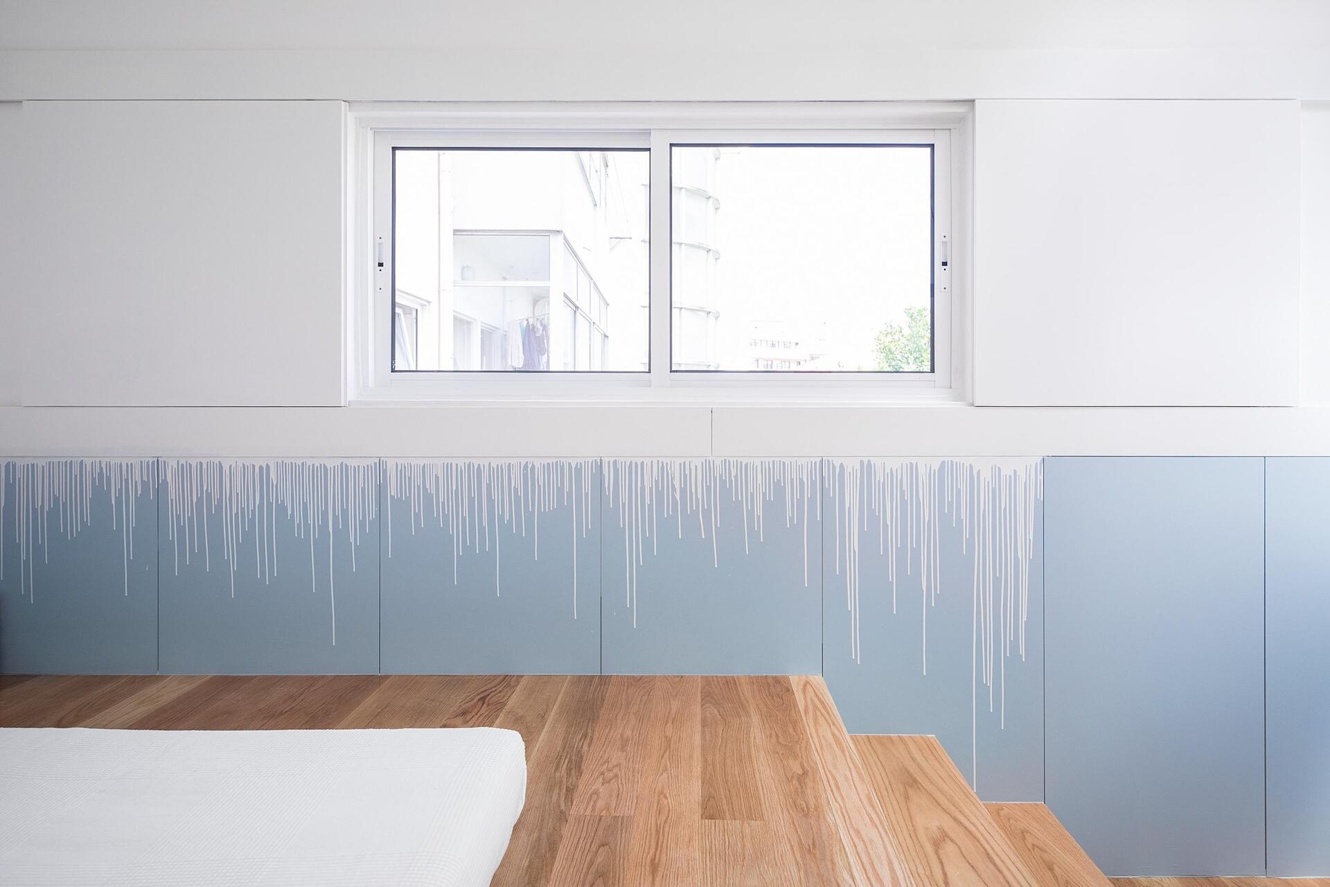 A tiny house bedroom with a raised wooden bed platform, built-in storage, and a soft blue and white drip-effect wall finish.