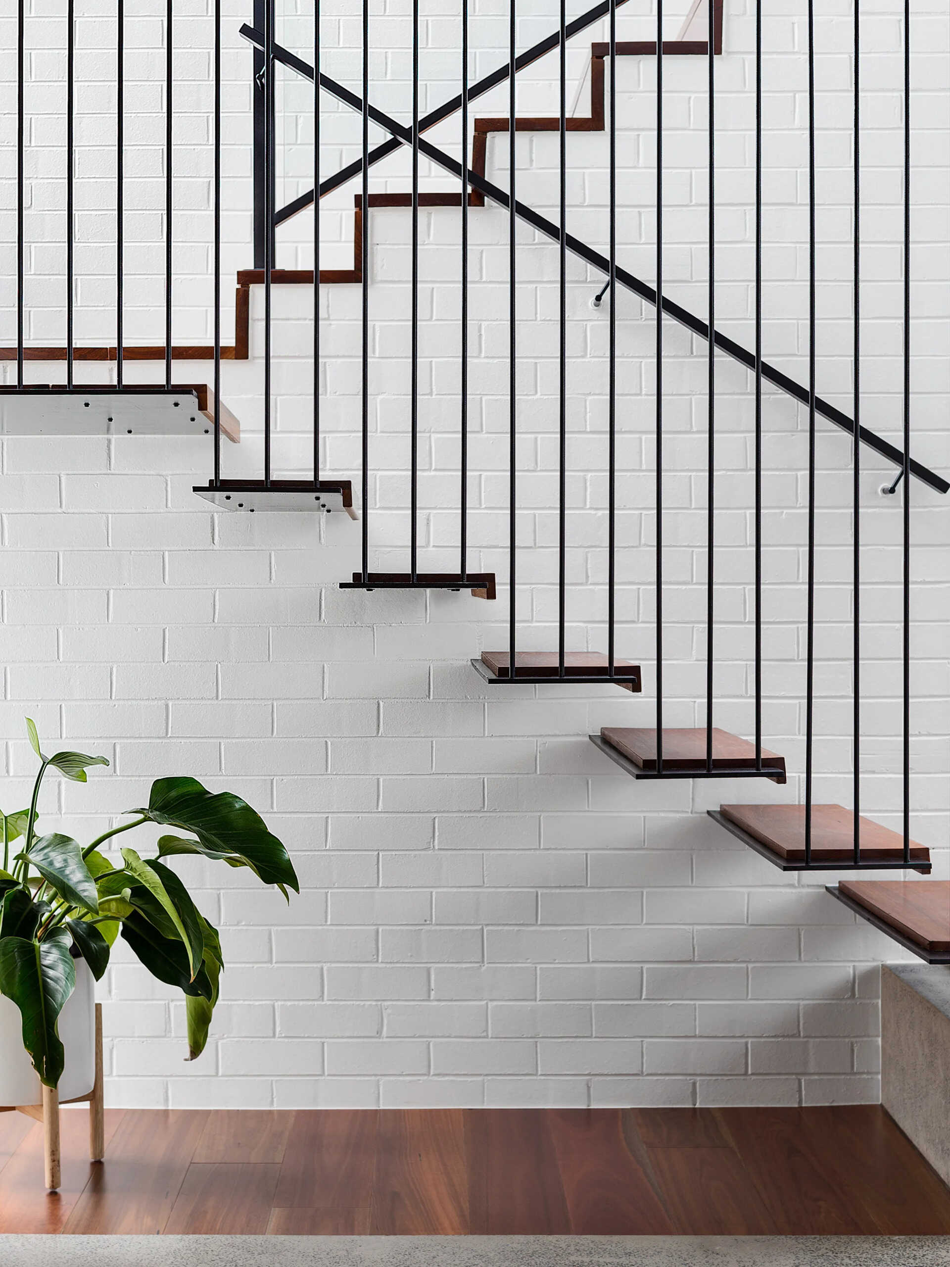 Concrete, steel, and wood stairs lead to the upper floor, transitioning from open treads to being part of a white-painted brick wall.