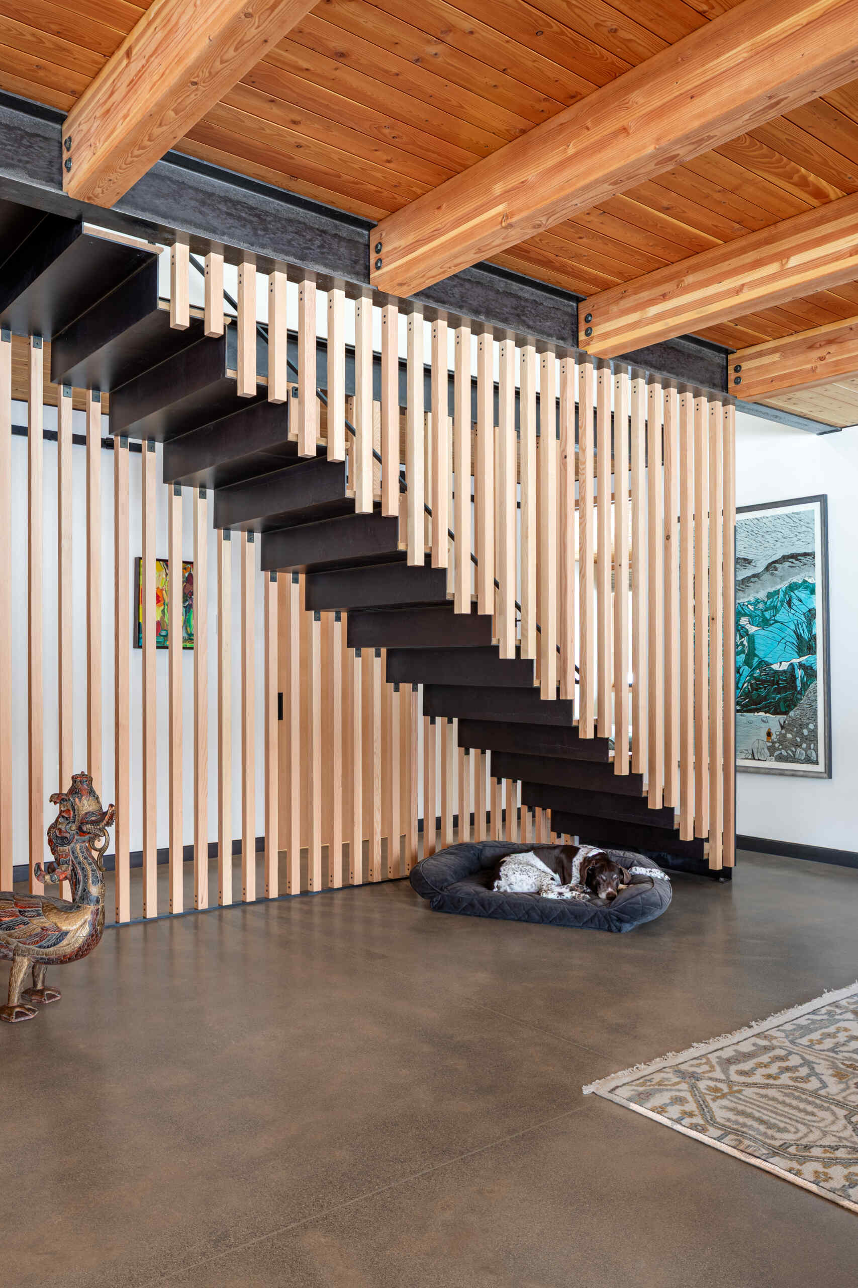 A sculptural stairway with black steel treads and a vertical wood slat screen, allowing light to move freely while adding texture and architectural interest.