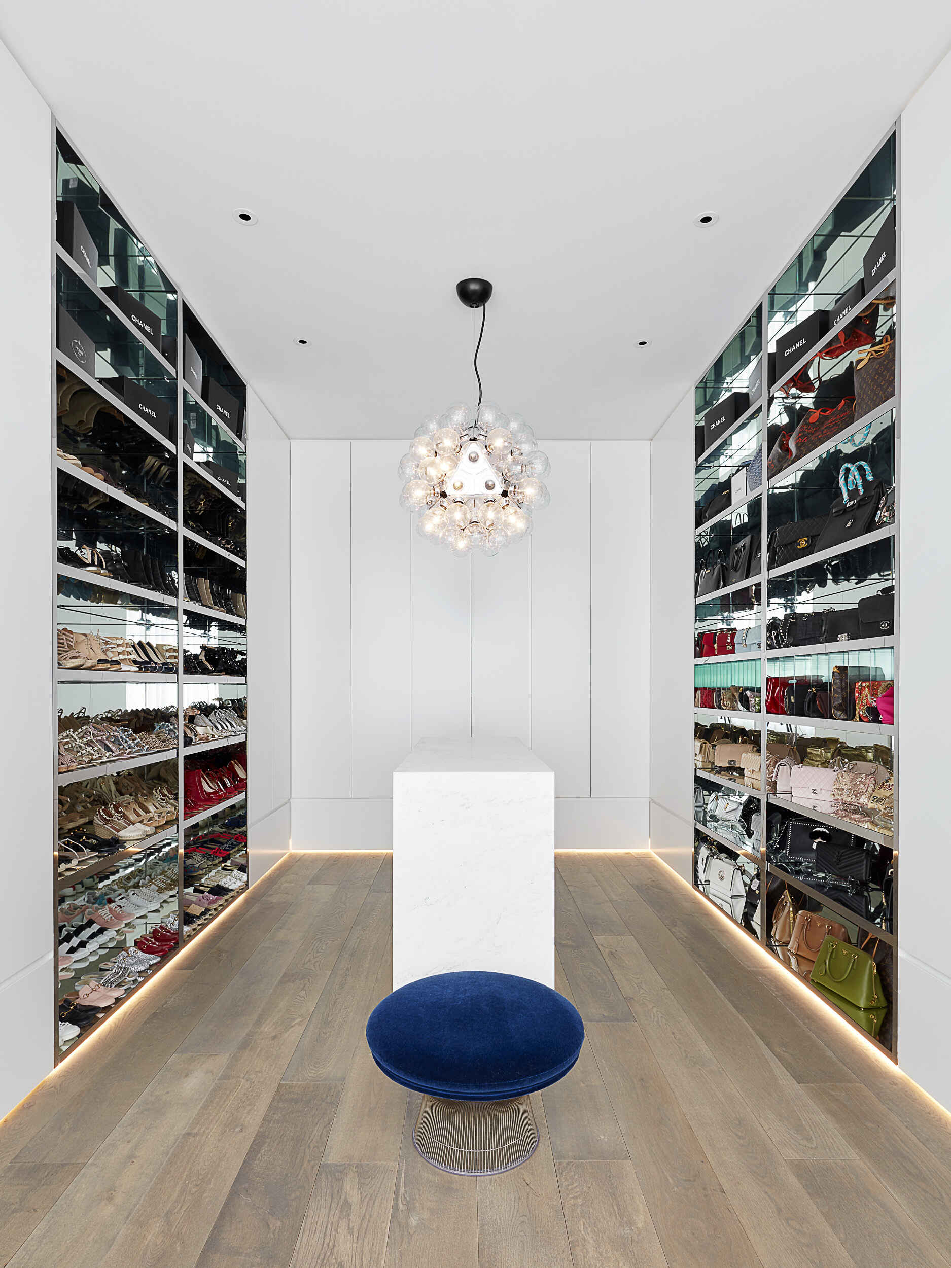 A dressing room with mirrored shelving and a central island combines smart storage with a polished look.