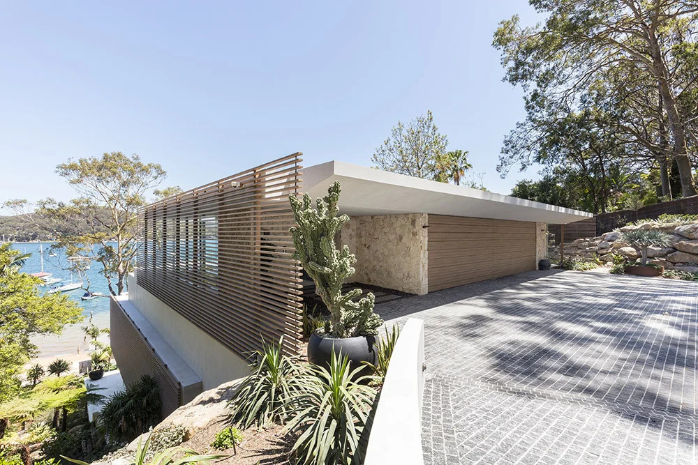 A terraced waterfront house steps down naturally on a steep slope with sandstone walls and a green roof.