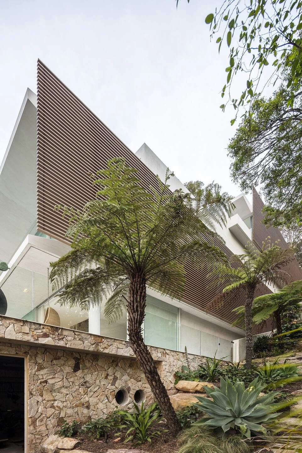 Cantilevered concrete slabs hover above a recessed stone podium, creating a floating, layered look that blends architecture with the site.