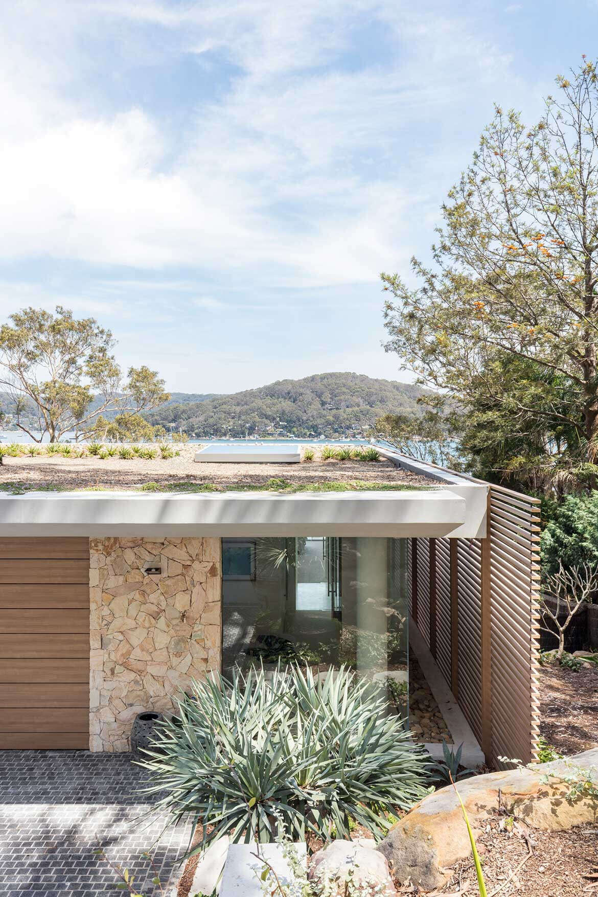 A terraced waterfront house steps down naturally on a steep slope with sandstone walls and a green roof.