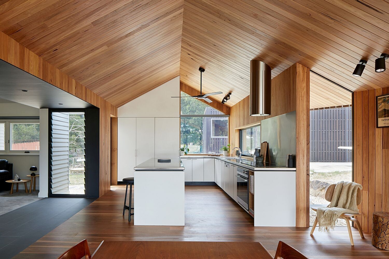 A large open room combines kitchen and dining in a warm, timber lined setting designed for relaxed country living.