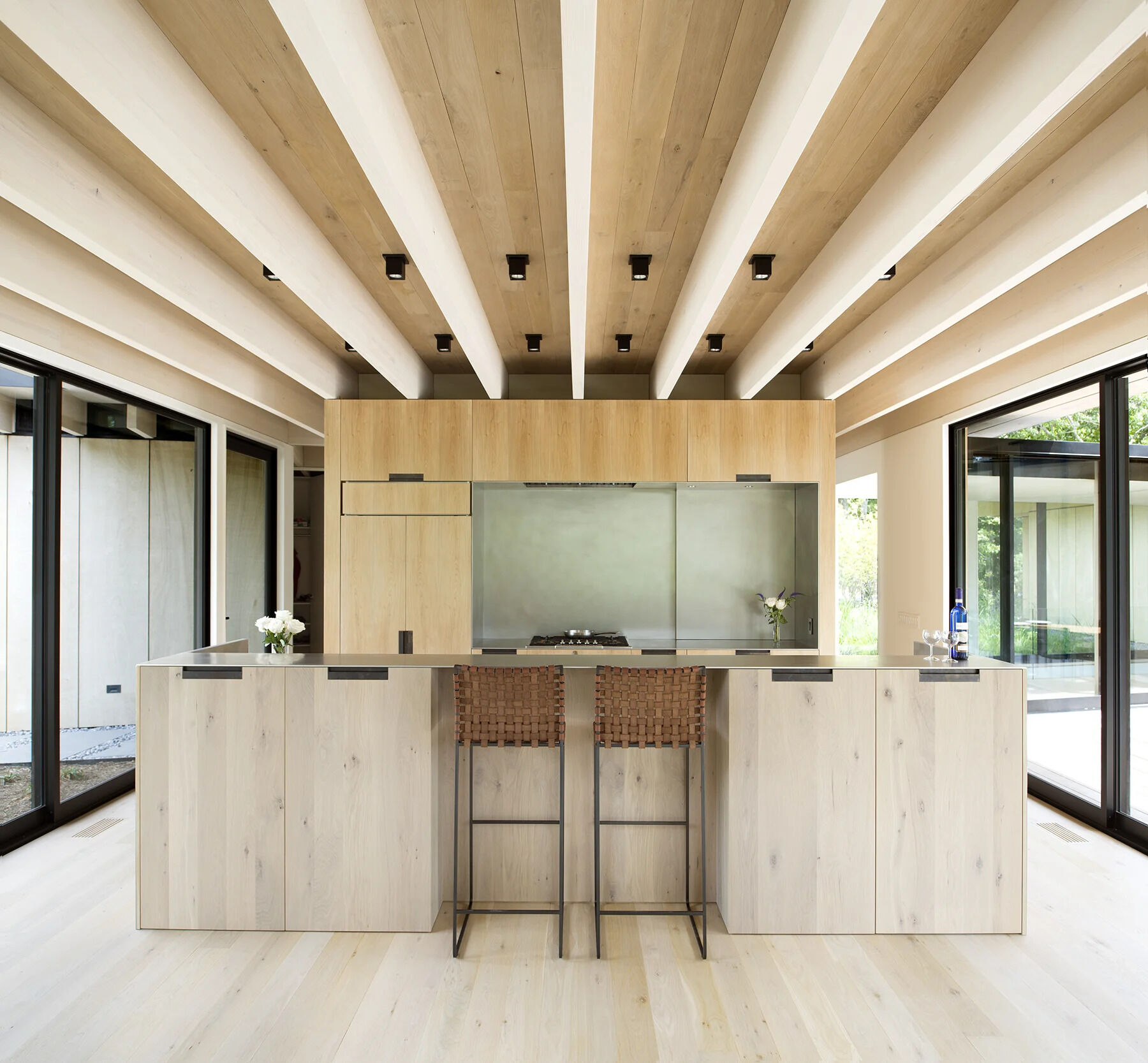 A minimalist kitchen with wood cabinetry and a generous island blends seamlessly with the home’s overall material palette.
