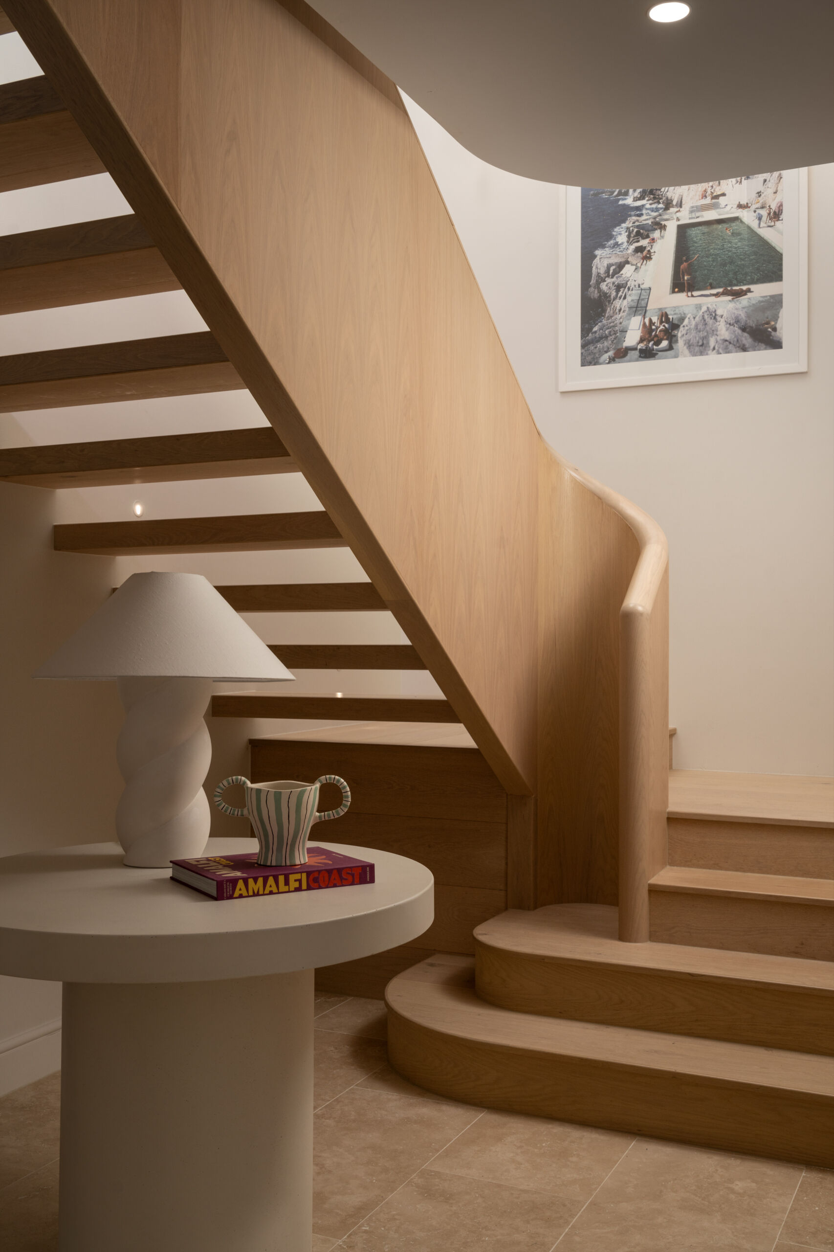 A curved oak and travertine staircase that mirrors the home’s soft Mediterranean lines.