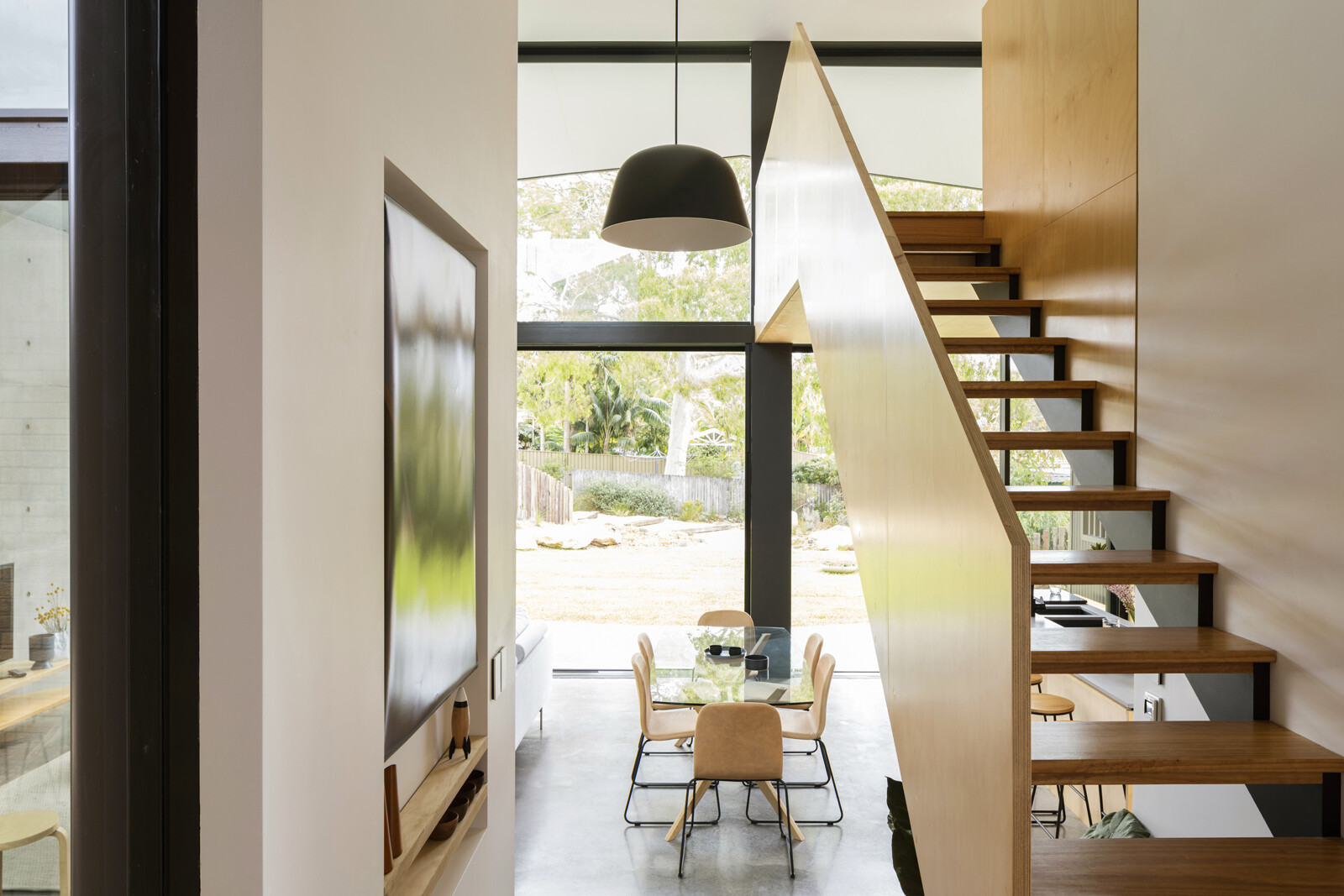 Off the hallway, a set of timber and steel stairs leads upward to a lofted area positioned above the kitchen. The stair continues the home’s material language while creating a clear vertical connection within the extension.