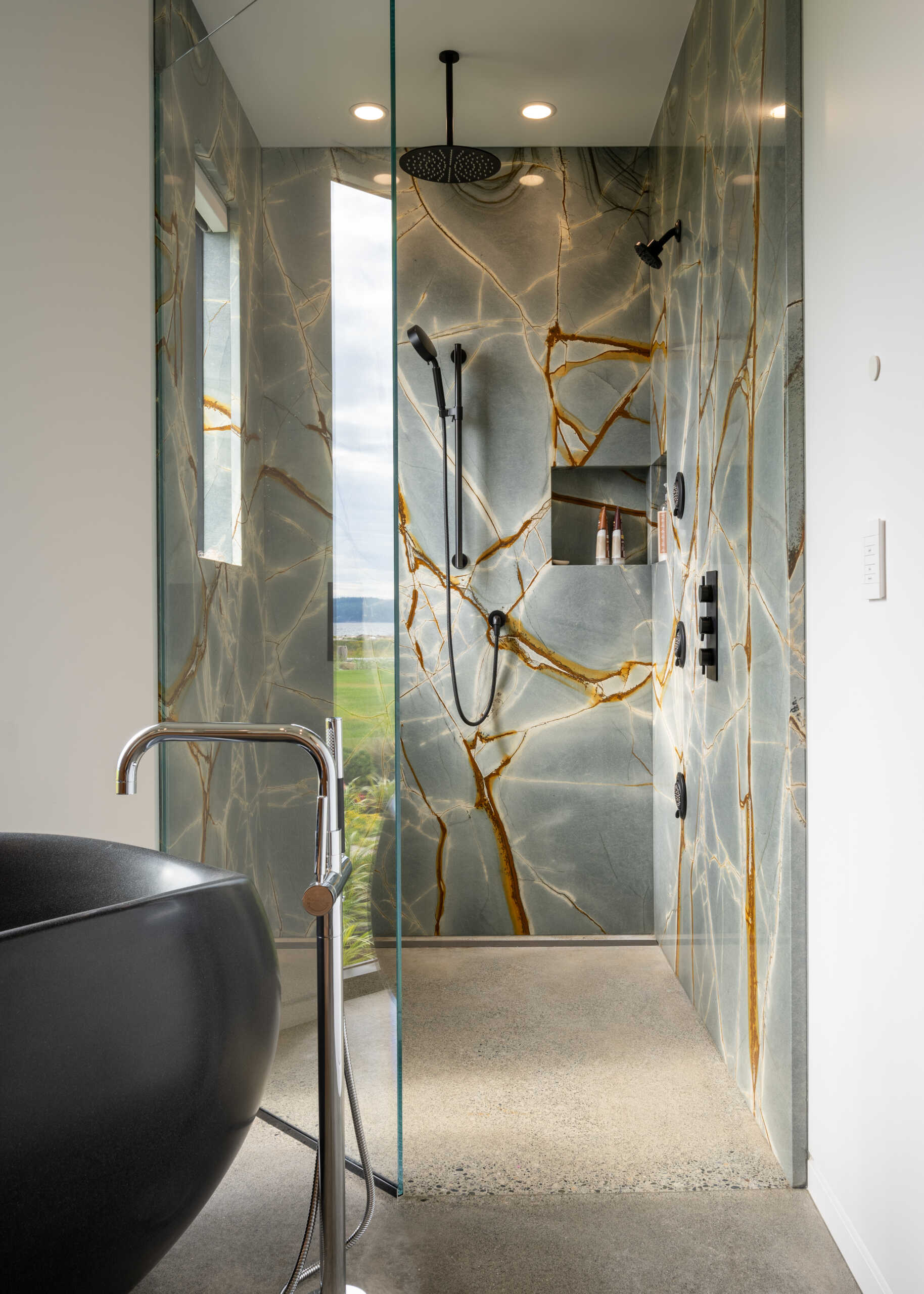 The primary bathroom includes a floating wood vanity with a freestanding sculptural black bathtub, and an eye-catching shower.