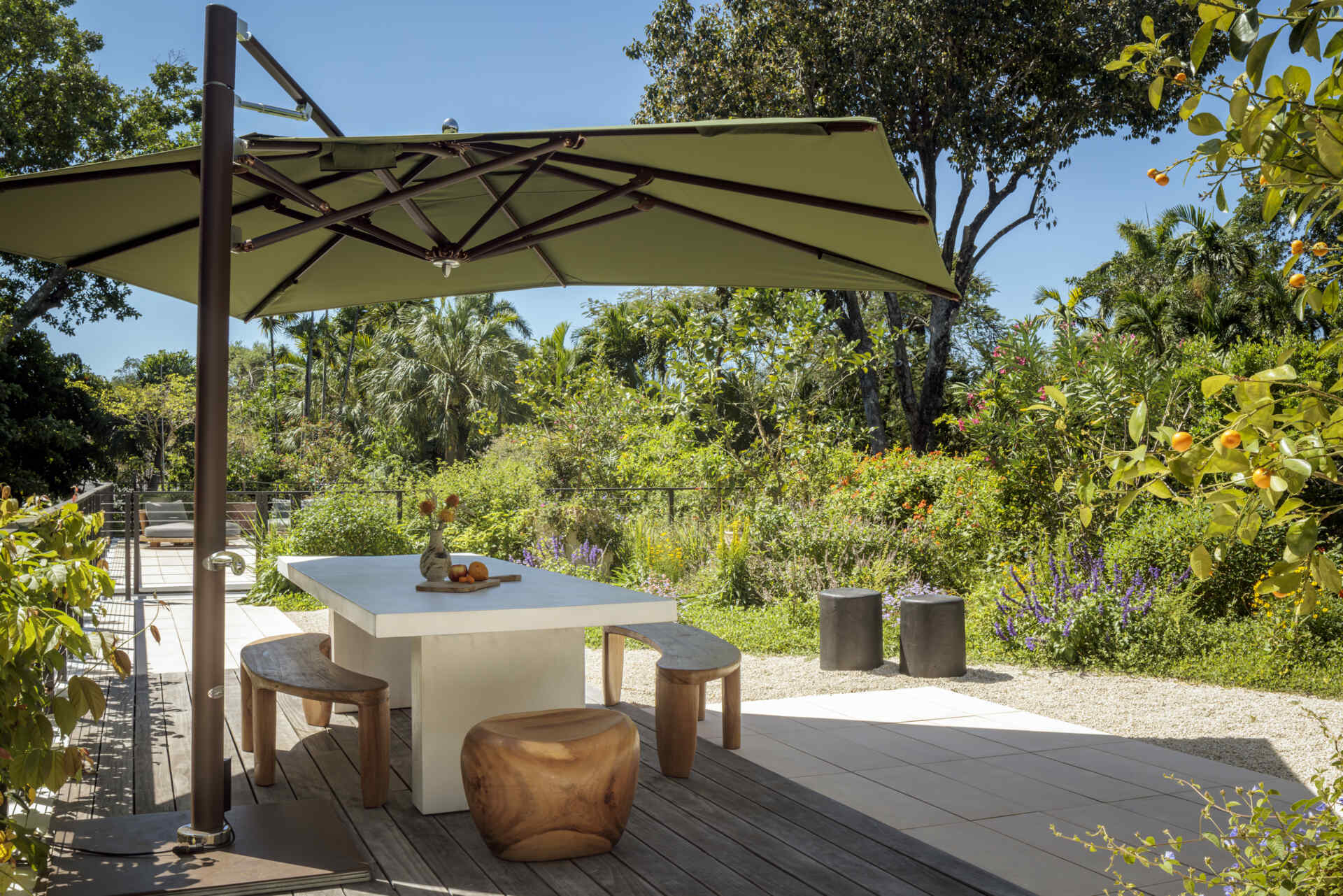 This modern living space opens seamlessly to the patio, turning outdoor areas into part of the room. A caramel velvet sofa and boucle chair add warmth and softness, while an oversized artwork adds color, and the shaded outdoor area invites relaxed meals and casual lounging surrounded by greenery.