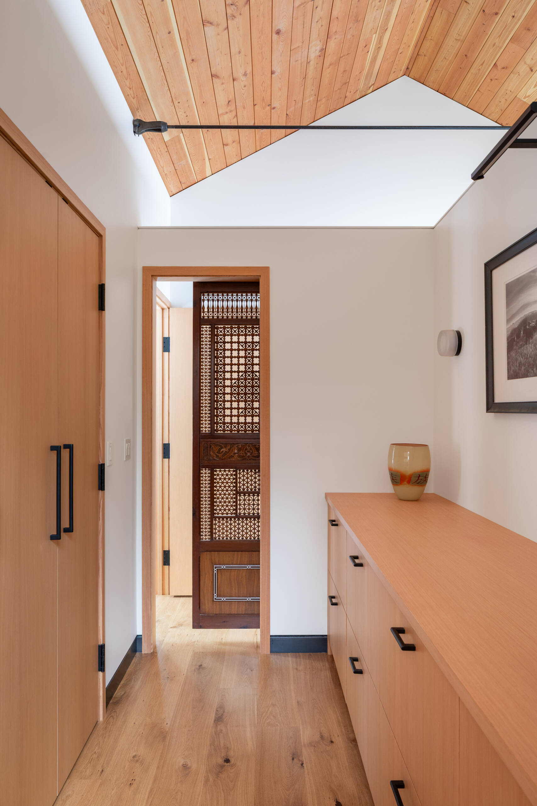 This primary suite feels serene and thoughtfully layered, mixing warm wood ceilings and pale built-ins with crisp white walls. A beautifully carved wood door adds a touch of old-world character, while the long dresser wall makes getting ready feel easy and uncluttered. In the bath, glossy white tile, a clean double vanity, and a sculptural soaking tub create a spa-like rhythm, softened by snowy views and gentle natural light.