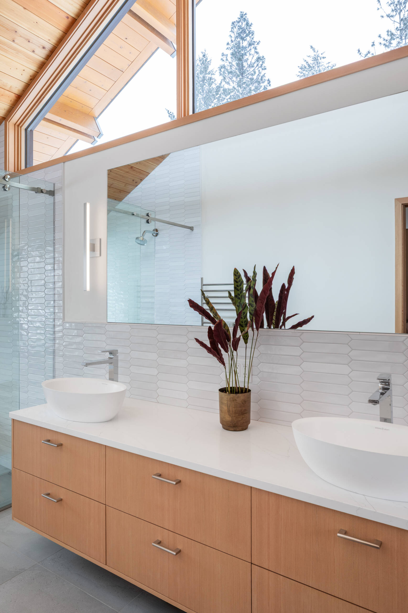 This primary suite feels serene and thoughtfully layered, mixing warm wood ceilings and pale built-ins with crisp white walls. A beautifully carved wood door adds a touch of old-world character, while the long dresser wall makes getting ready feel easy and uncluttered. In the bath, glossy white tile, a clean double vanity, and a sculptural soaking tub create a spa-like rhythm, softened by snowy views and gentle natural light.