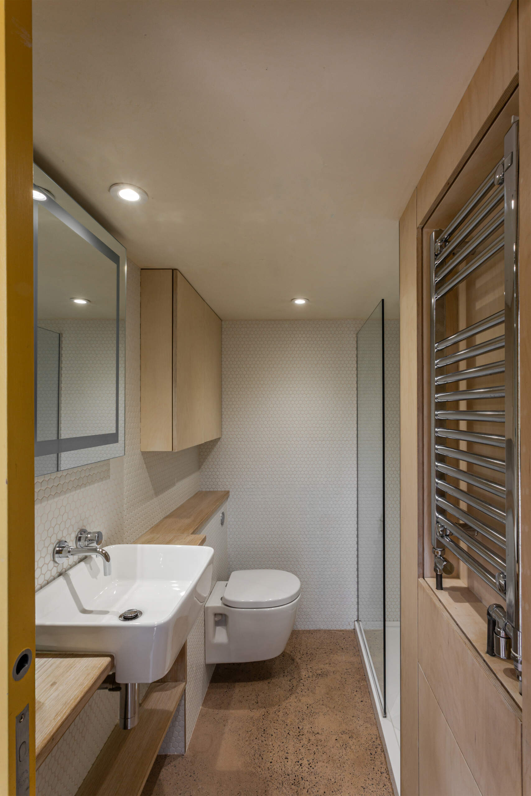 El baño con ducha está completamente contenido dentro de un núcleo de madera contrachapada. Las paredes de azulejos, las cálidas superficies de madera y un piso continuo de concreto rosa crean un espacio tranquilo e íntimo.