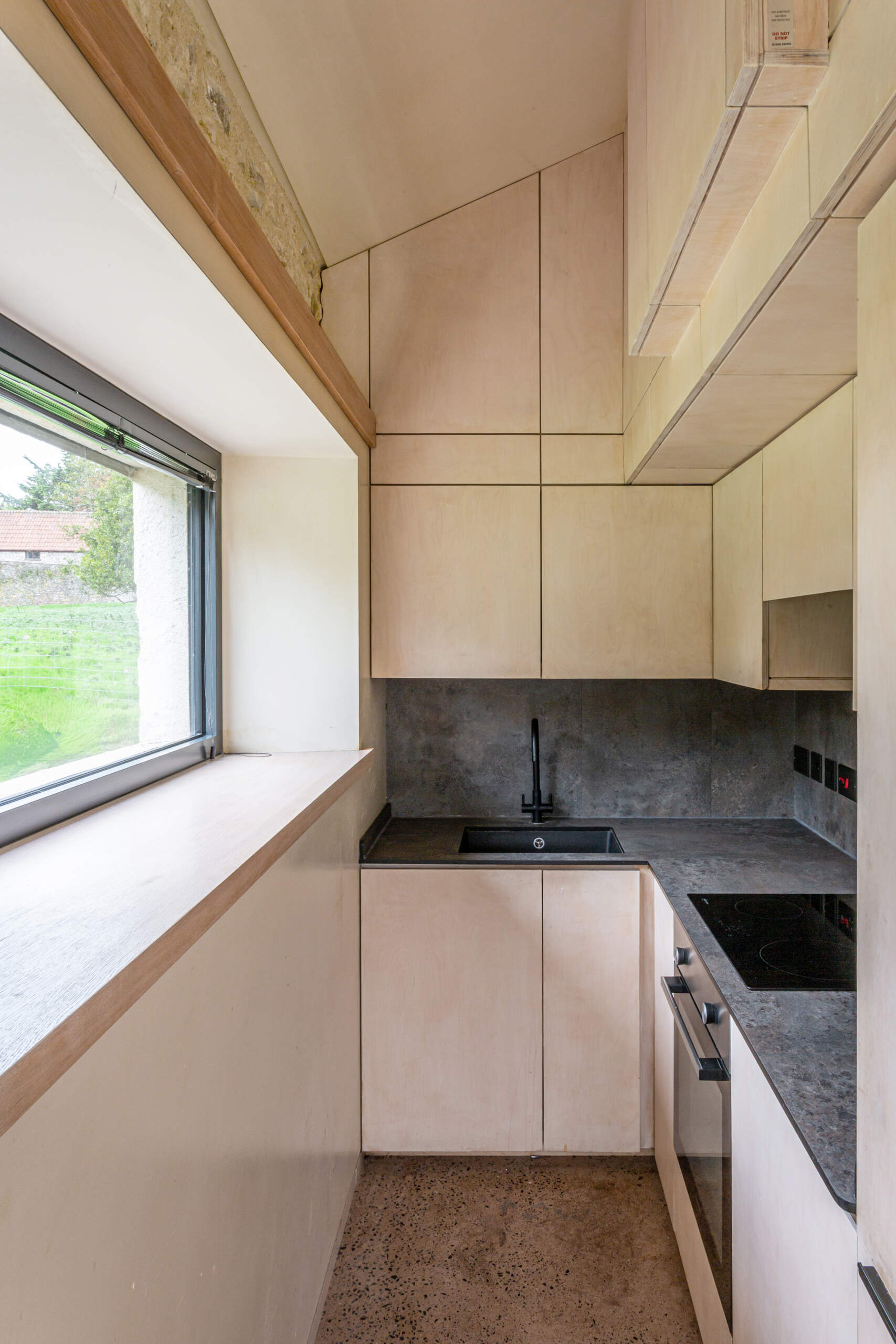 La cocina está alojada dentro de una estructura de madera contrachapada que forma el núcleo del interior. Esta inserción controlada integra almacenamiento, paneles y servicios clave en una sola acción. Este enfoque mantiene la pequeña huella abierta y tranquila al mismo tiempo que le da al espacio su propio carácter cuidadosamente diseñado.