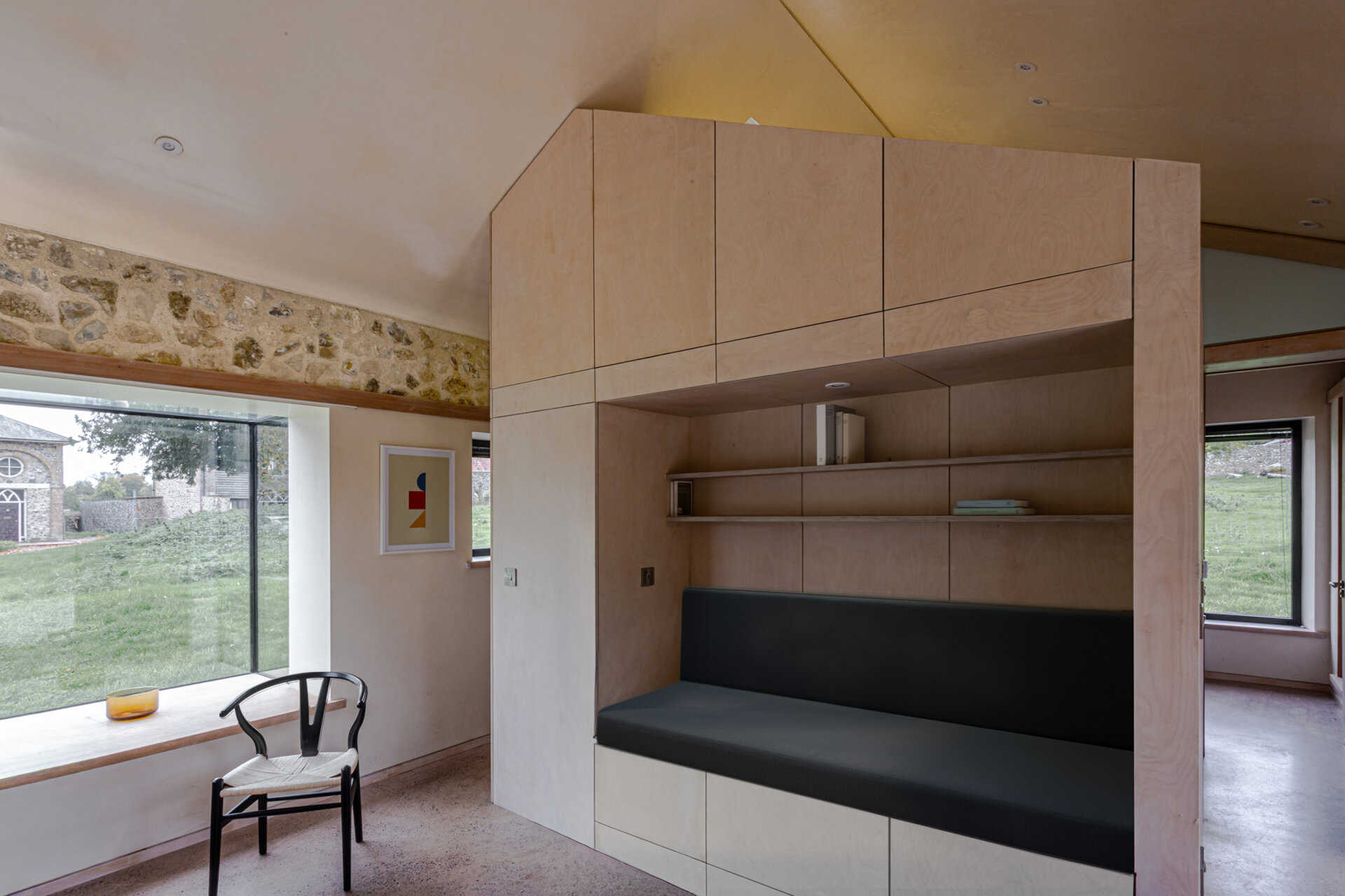 Dentro de esta pocilga reconvertida, las rugosas paredes de piedra permanecen expuestas, envolviendo el espacio con textura e historia. El nuevo volumen de madera contrachapada está claramente ubicado dentro de la carcasa, manteniendo la funcionalidad clave y al mismo tiempo permitiendo que las paredes perimetrales permanezcan sin cambios. Los asientos y estantes incorporados añaden comodidad práctica sin añadir peso visual.