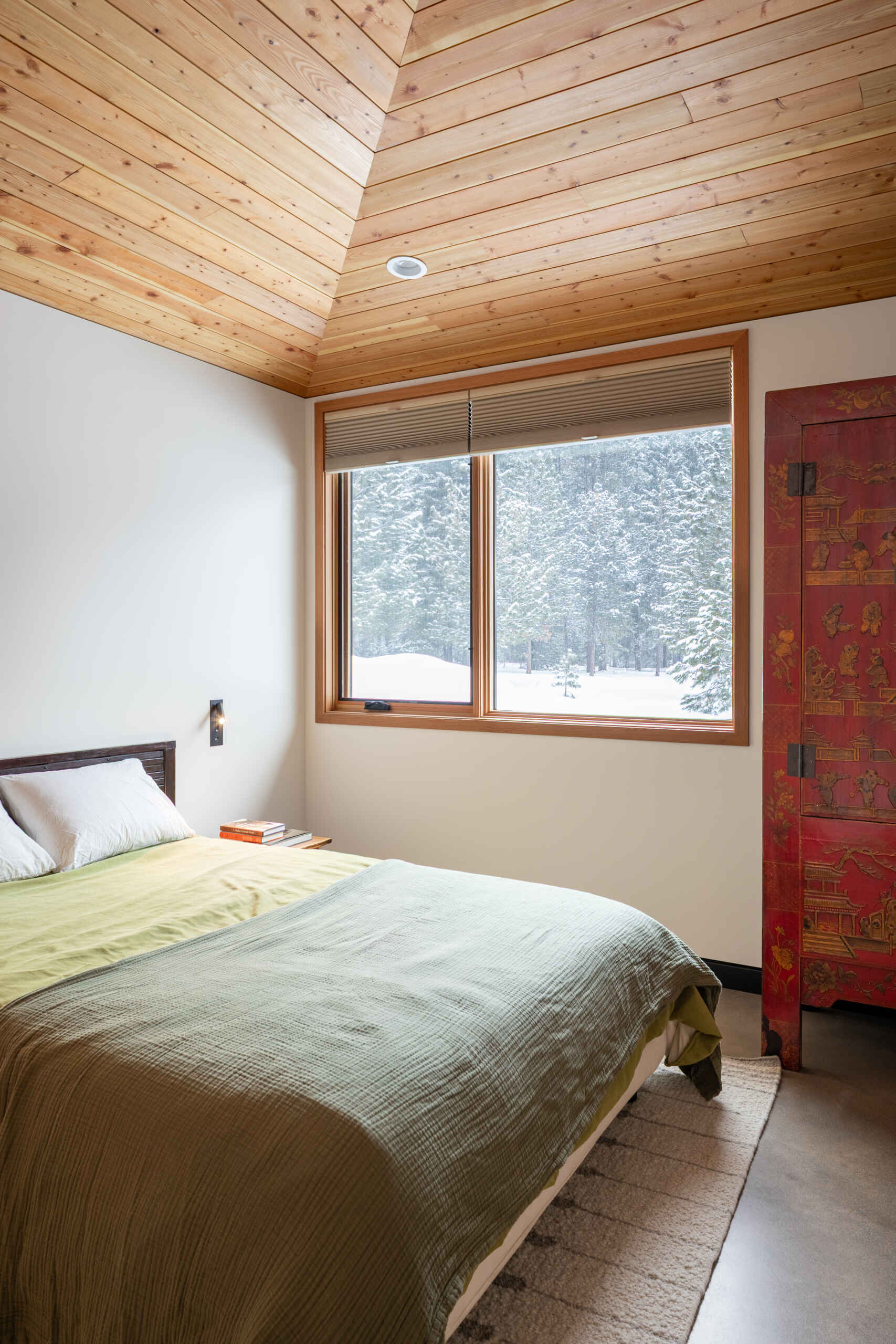Simple, inviting bedrooms with warm wood ceilings, soft white walls, and thoughtful personal touches that create calm spaces connected to forest views.