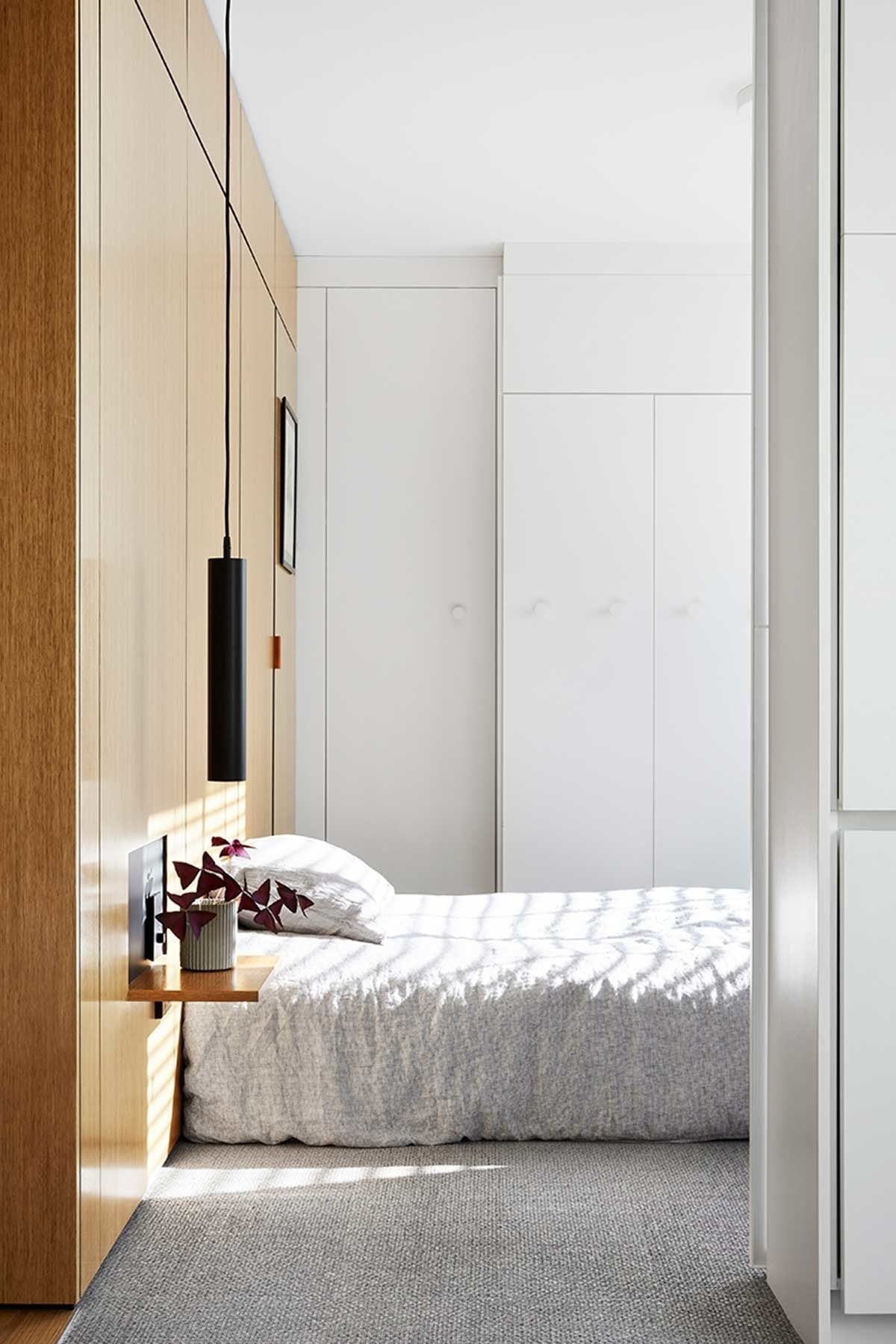 Timber wall cladding forms a headboard, bedside table and hidden bathroom door in this minimalist bedroom design.