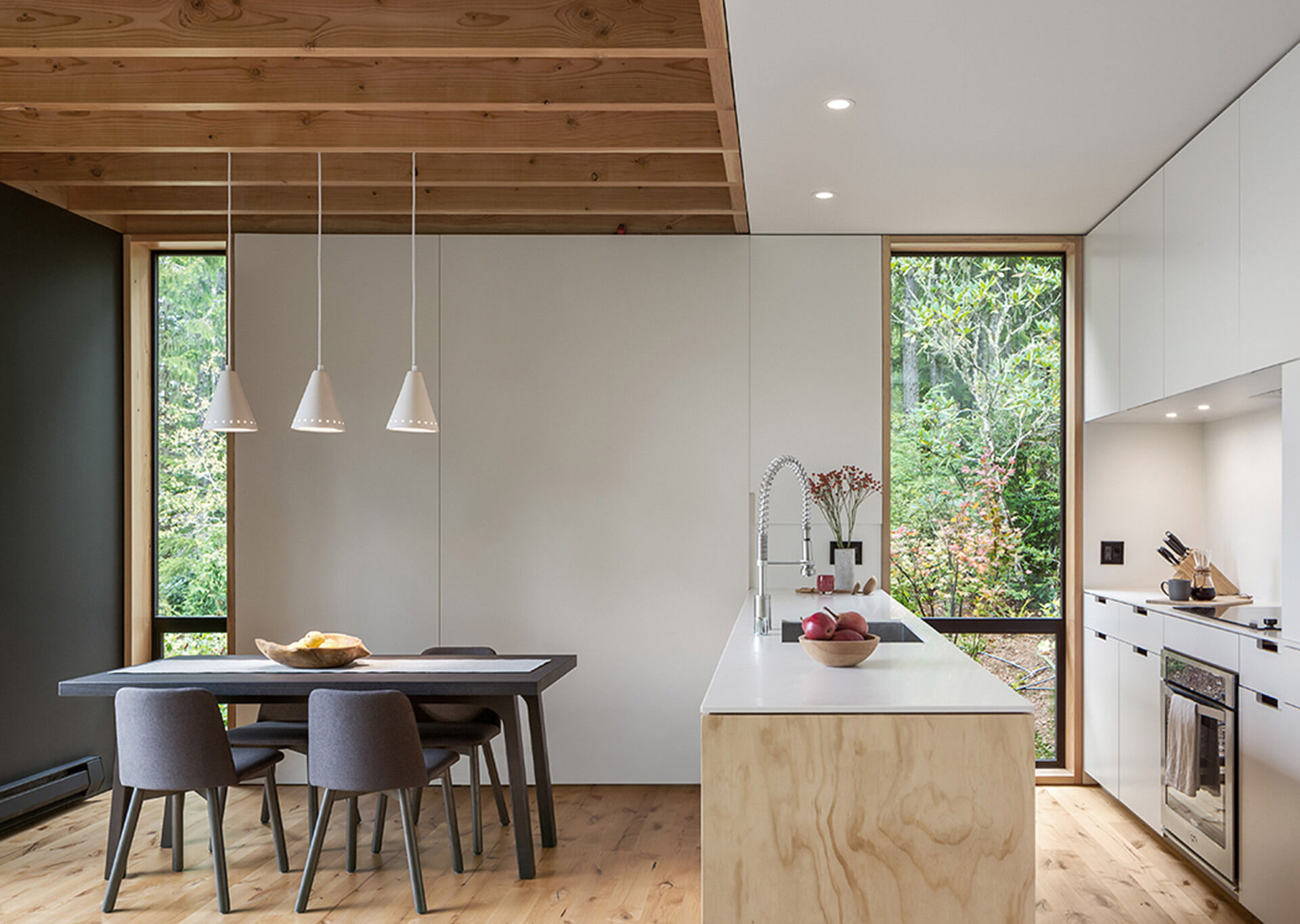 A bright white cabin kitchen with simple pendant lights and sweeping forest and water views.