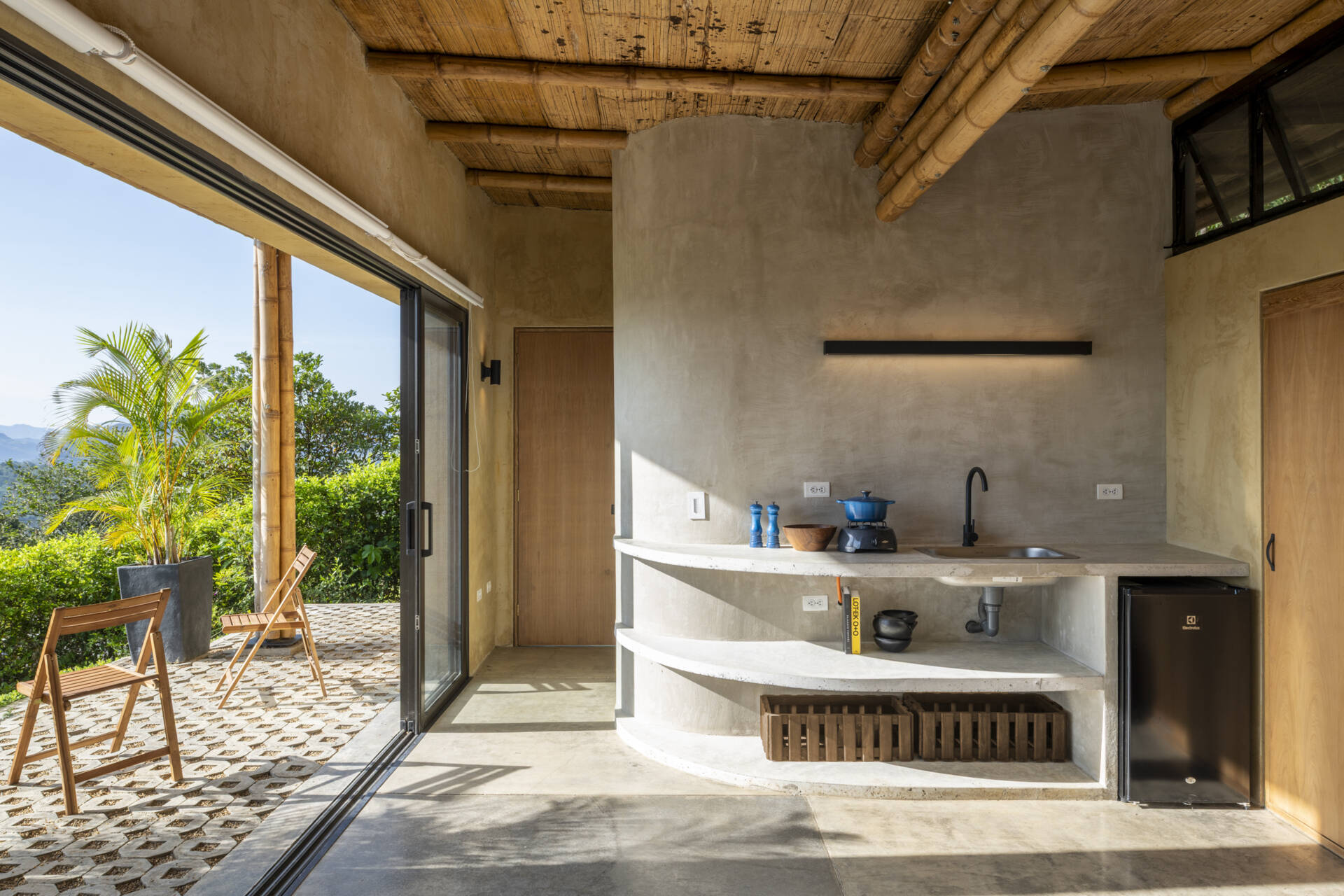 This Colombian home reimagines rural architecture with a butterfly roof that collects rainwater, bamboo-and-steel structural details, and an open interior where the bedroom, kitchenette, and a hidden curved-wall bathroom blend seamlessly, creating a sustainable, modern, and deeply connected living experience.