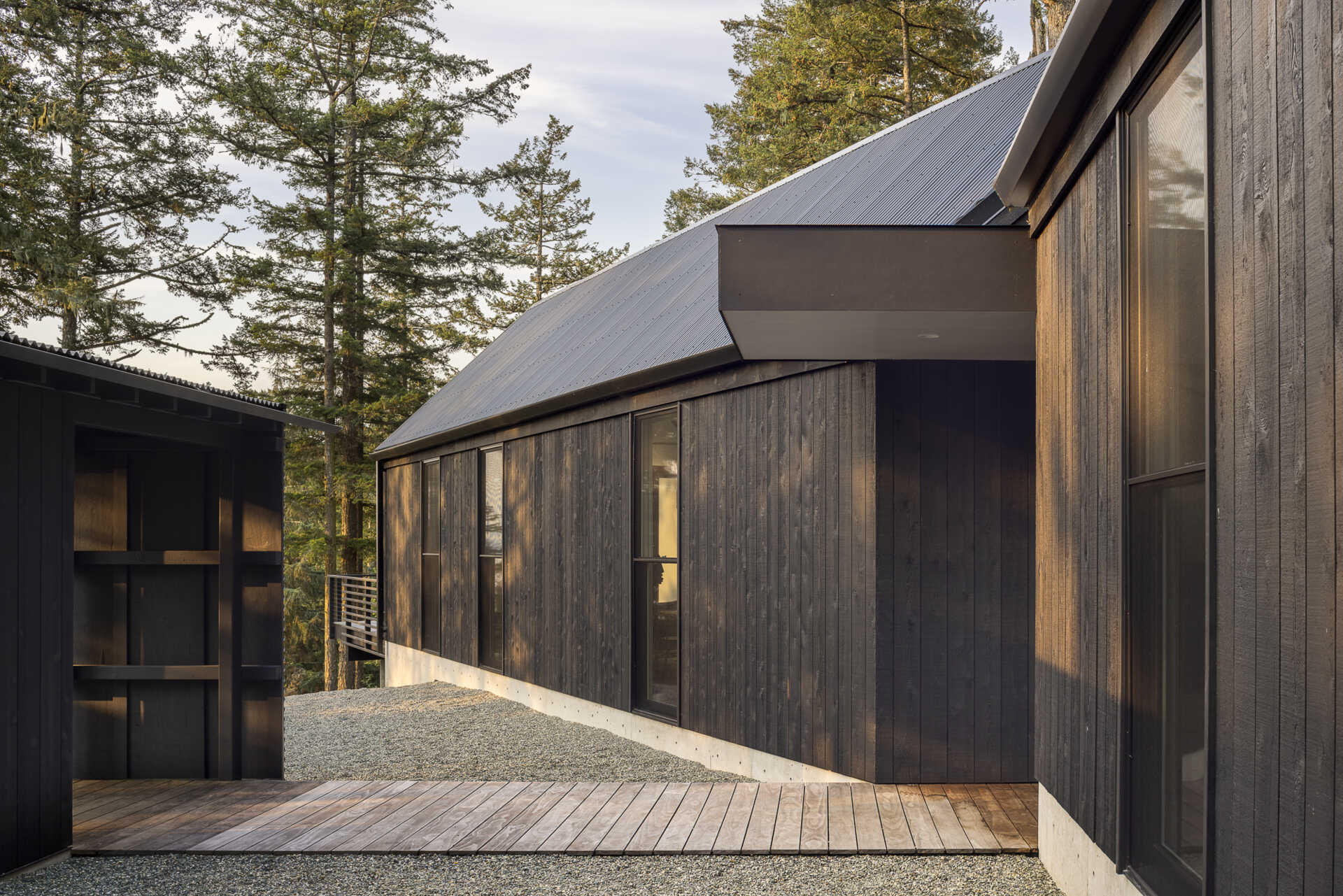 A minimalist gabled home on Orcas Island finished in dark weathered wood, set among old growth trees with layered views in every direction.