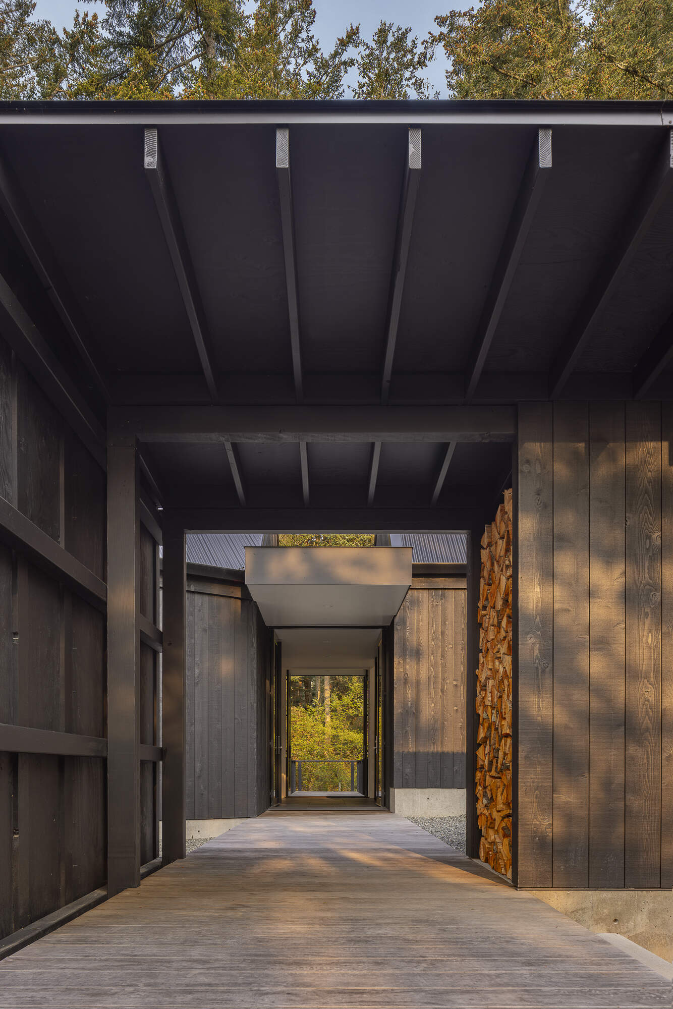 A minimalist gabled home on Orcas Island finished in dark weathered wood, set among old growth trees with layered views in every direction.